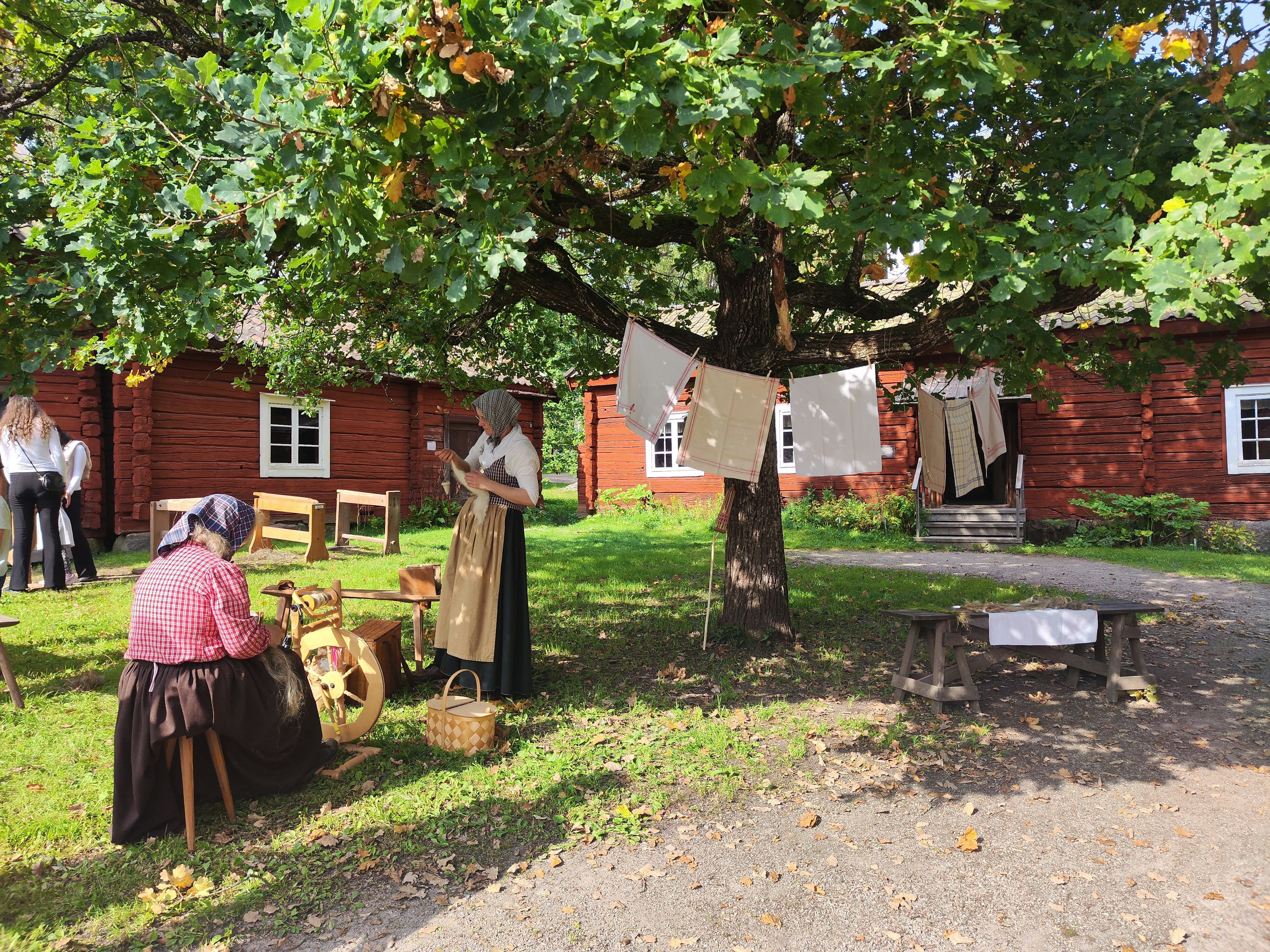 Szene von Menschen in traditioneller Kleidung, die sich unter einem Baum vor roten Häusern versammeln