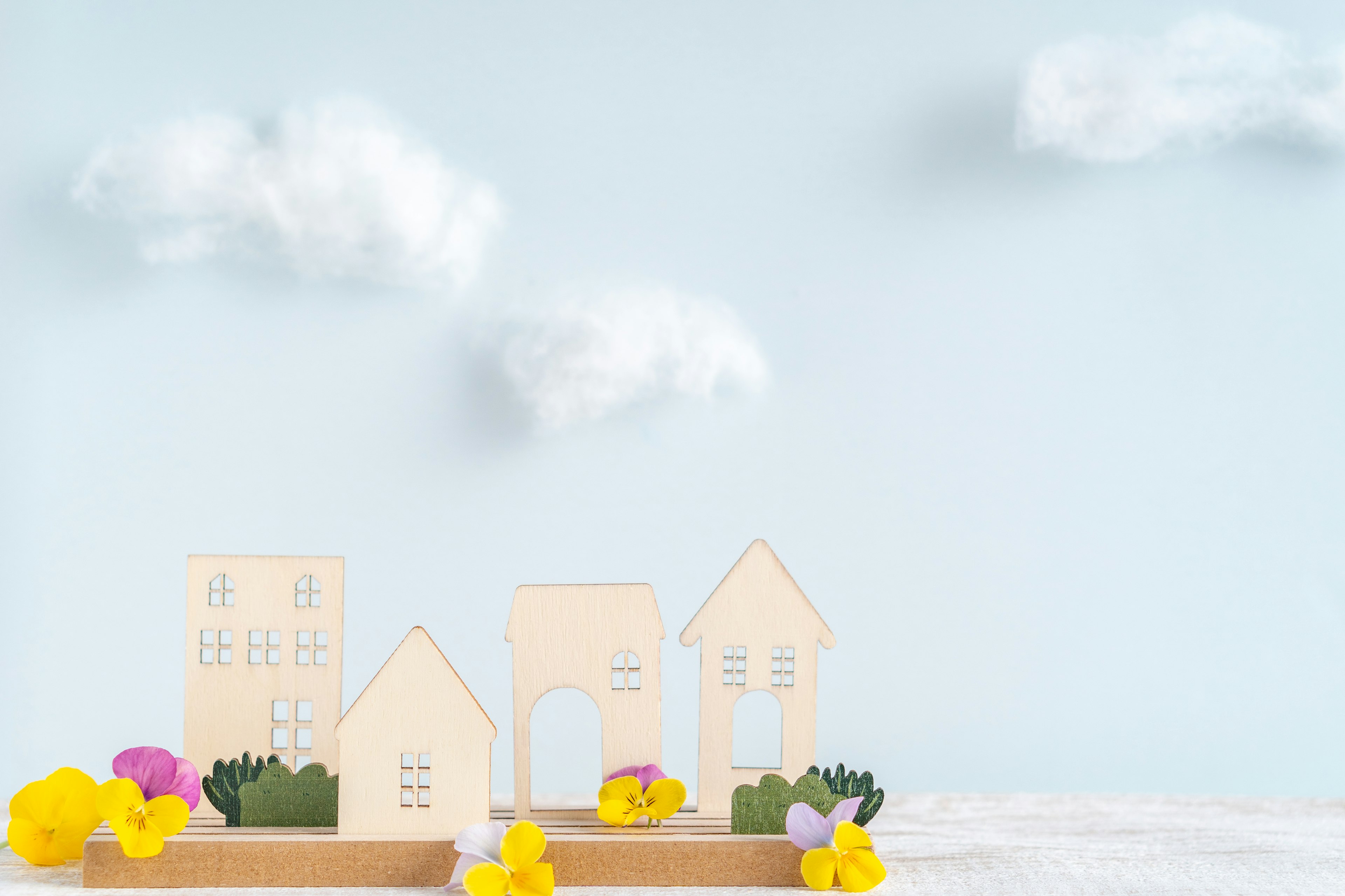 Modelos de casas de madera dispuestos bajo un cielo azul con flores coloridas