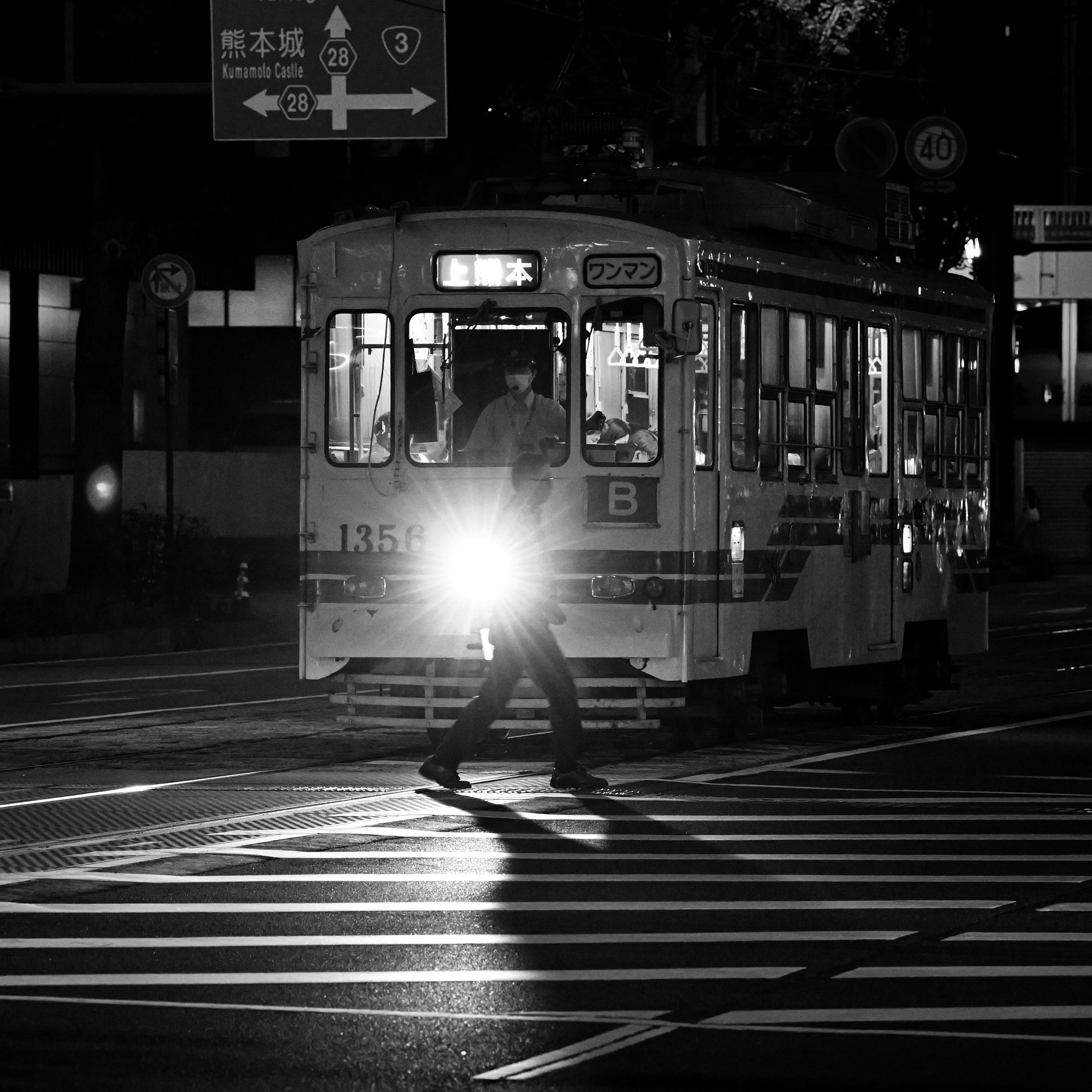 A person walking across a zebra crossing with a tram approaching at night