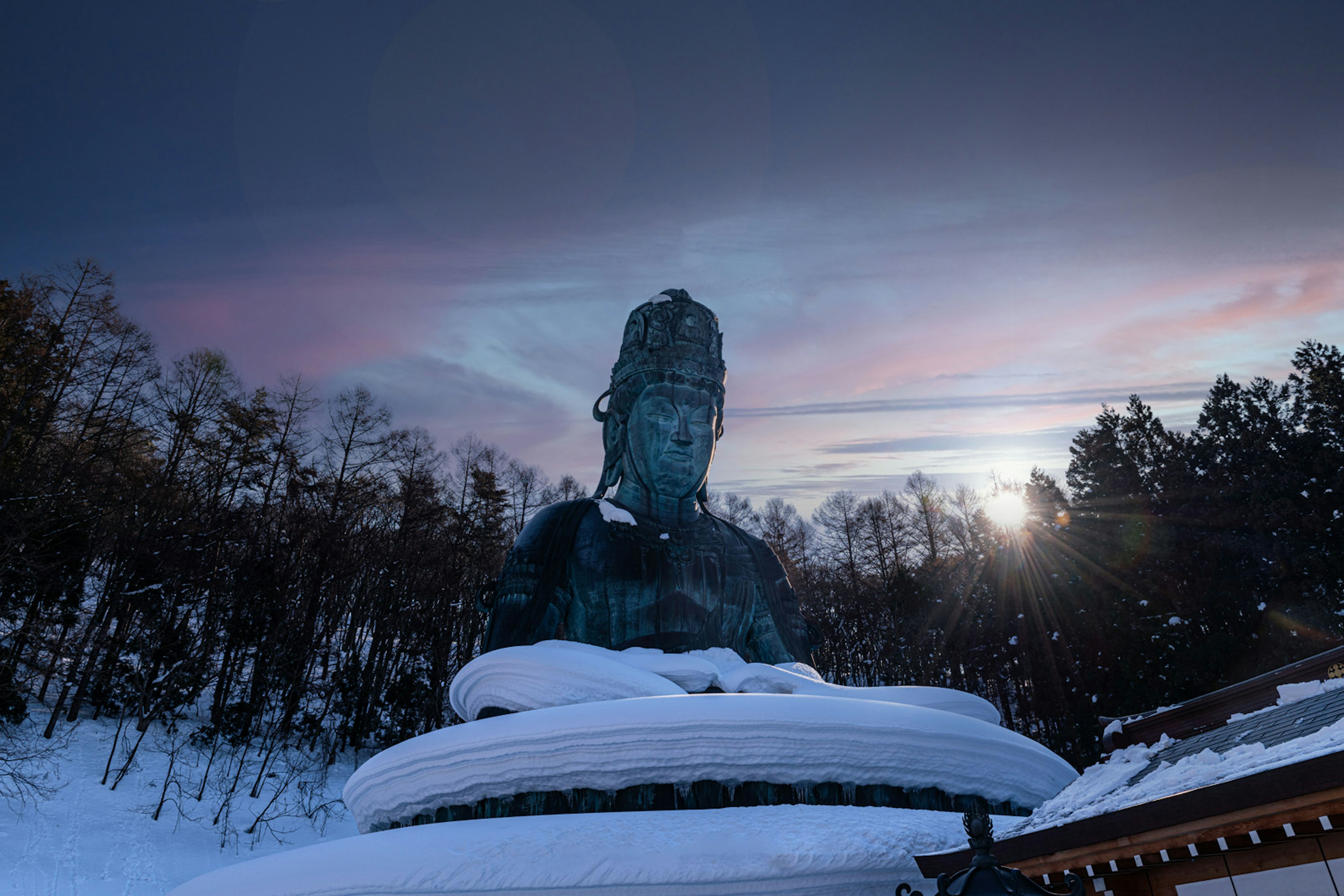 雪に覆われた大仏の像と美しい夕焼けの空