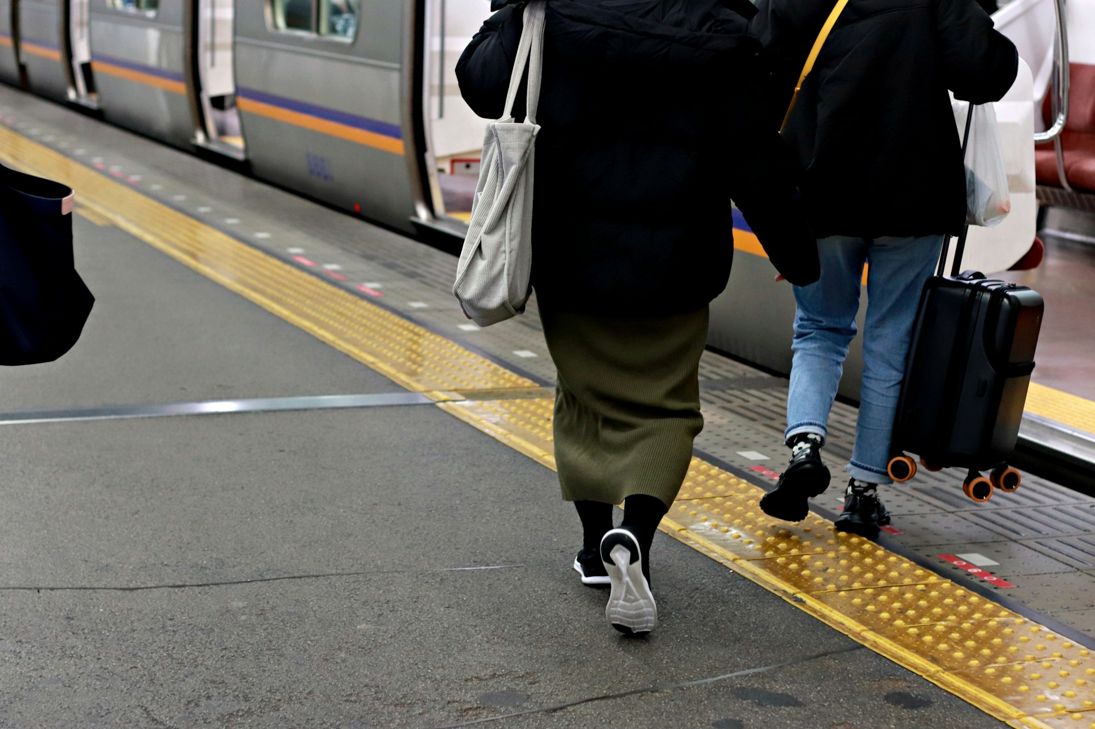 Two people walking on a train platform with luggage