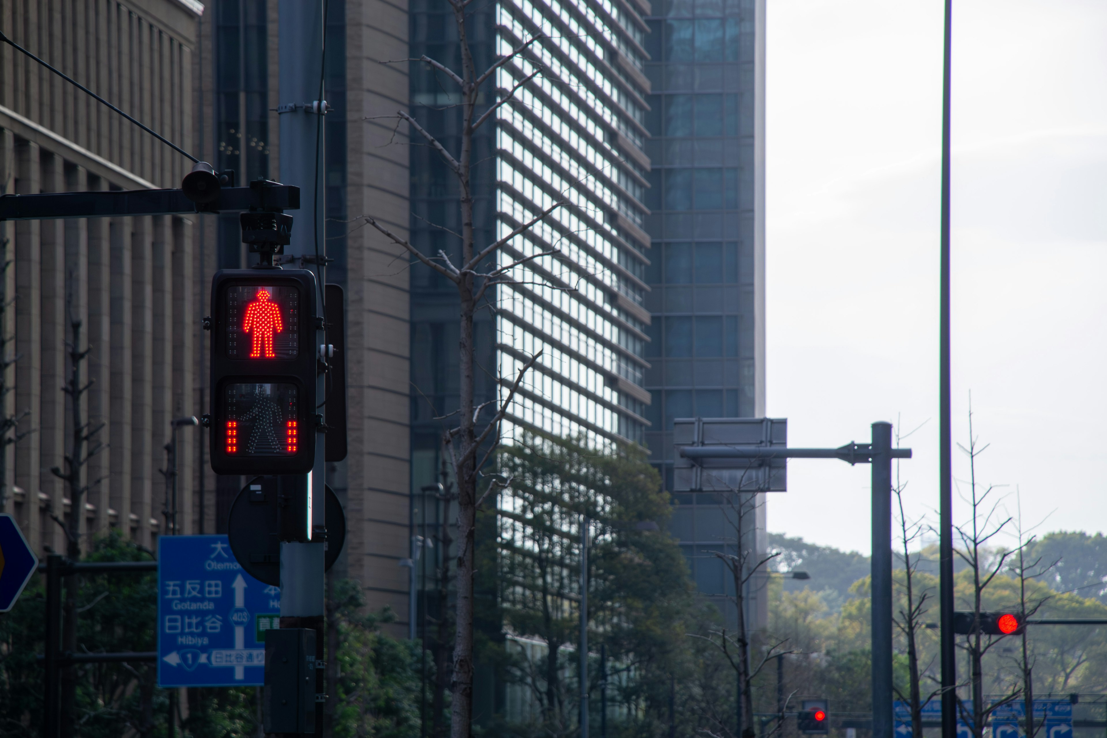 Lampu lalu lintas pejalan kaki merah dengan gedung modern di latar belakang