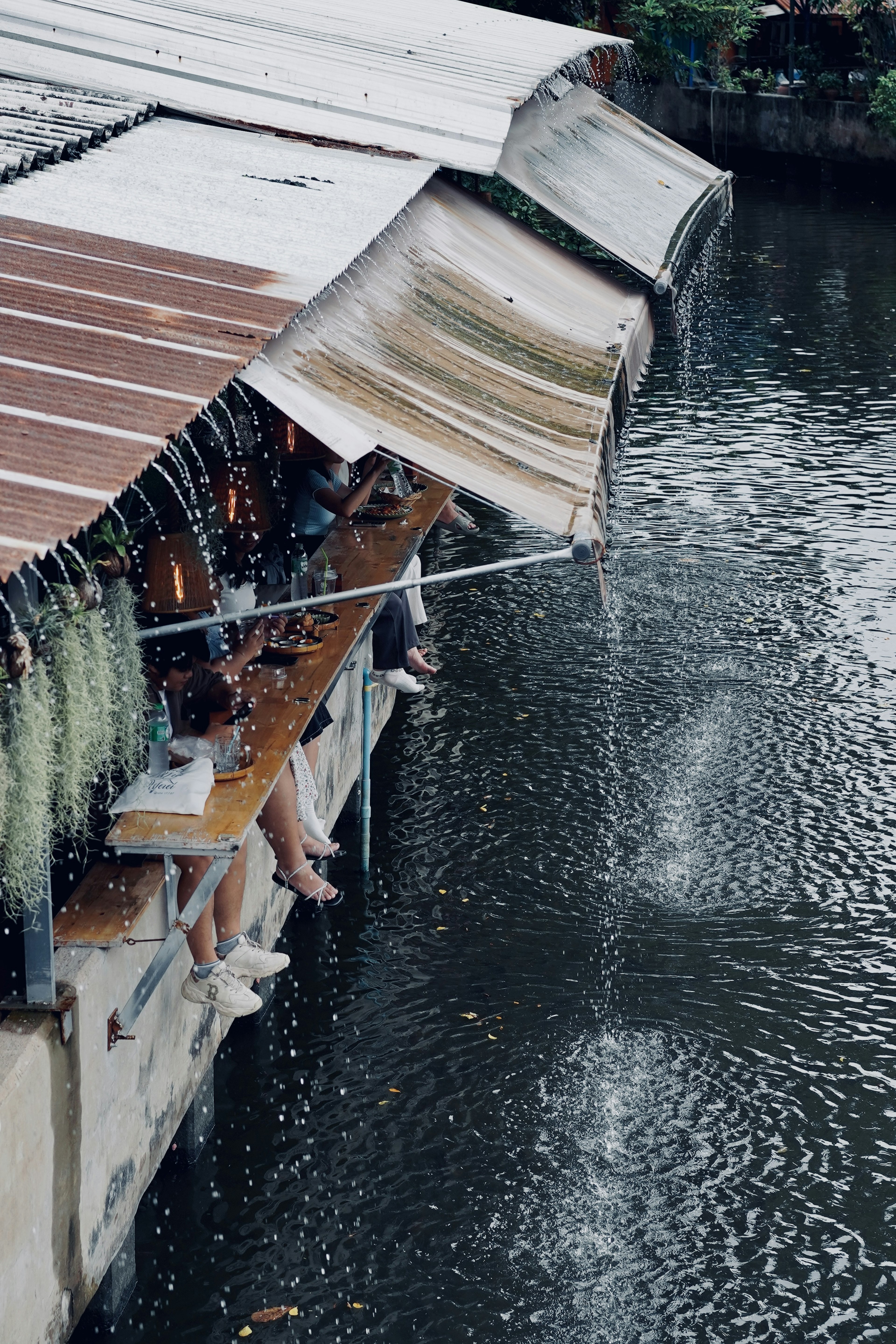 川の上に建てられた店舗の屋根から水が流れ落ちる風景