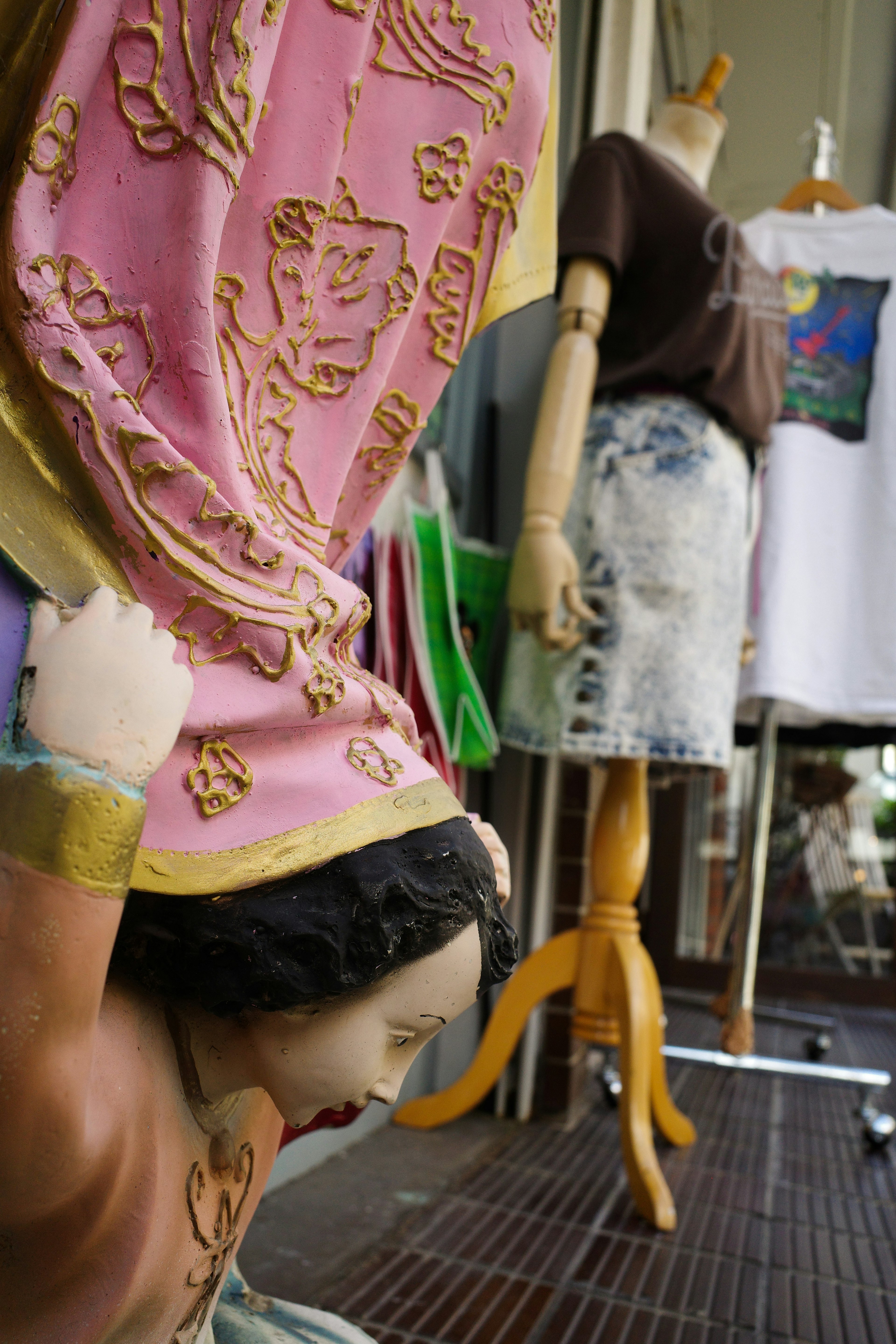 A colorful dressed doll in the foreground with a mannequin wearing clothes in the background