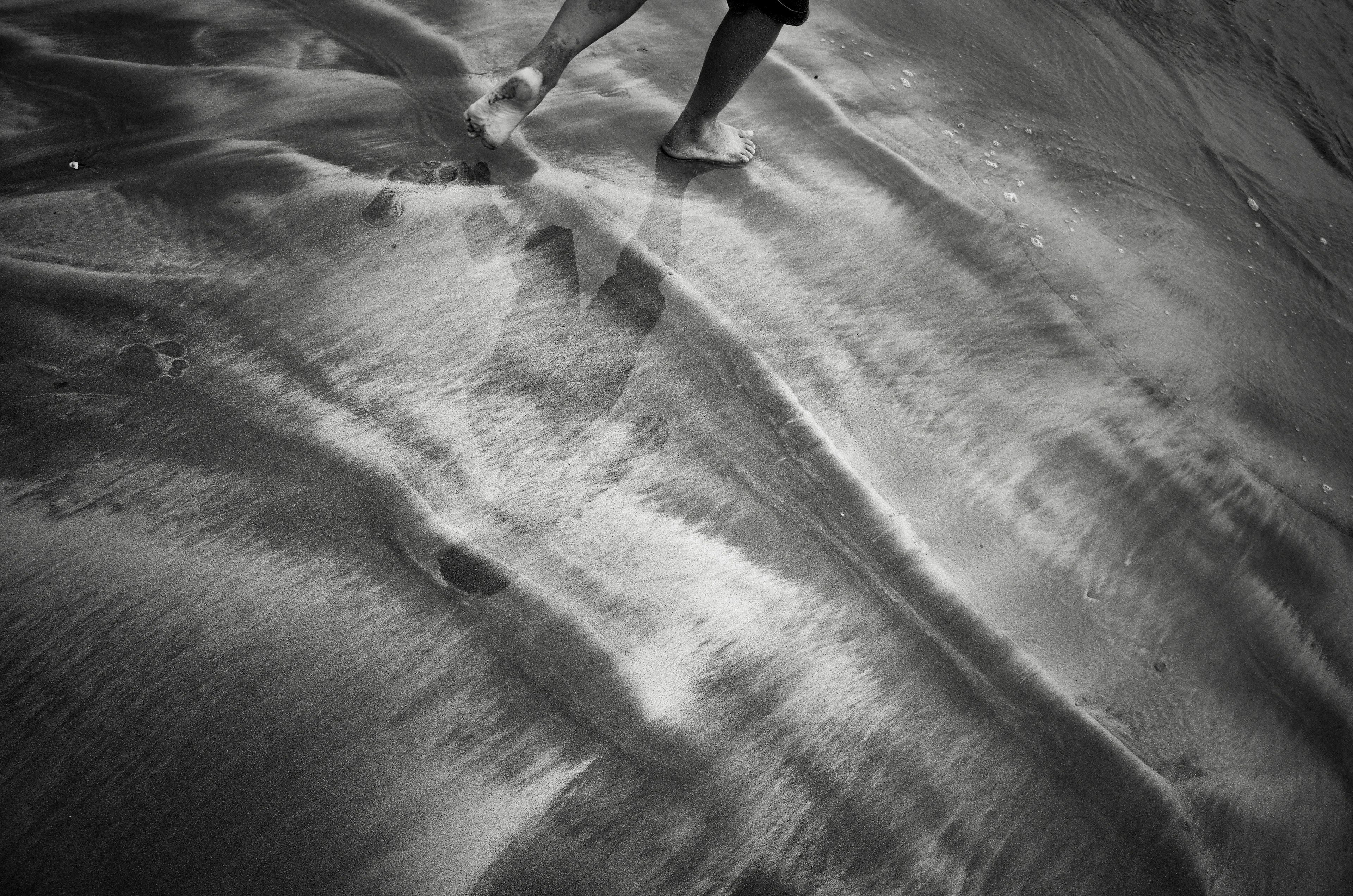 Barefoot person walking on the beach with wave patterns