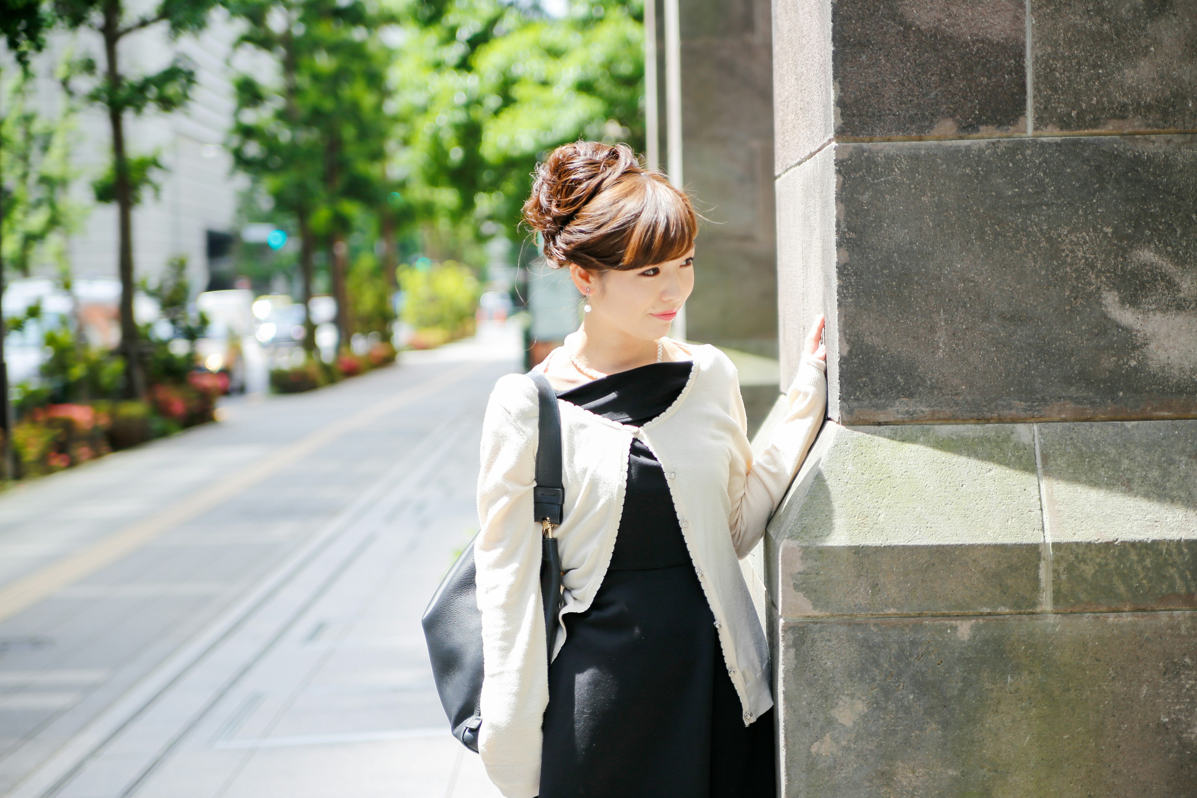 A woman in a black dress and white jacket standing at a street corner