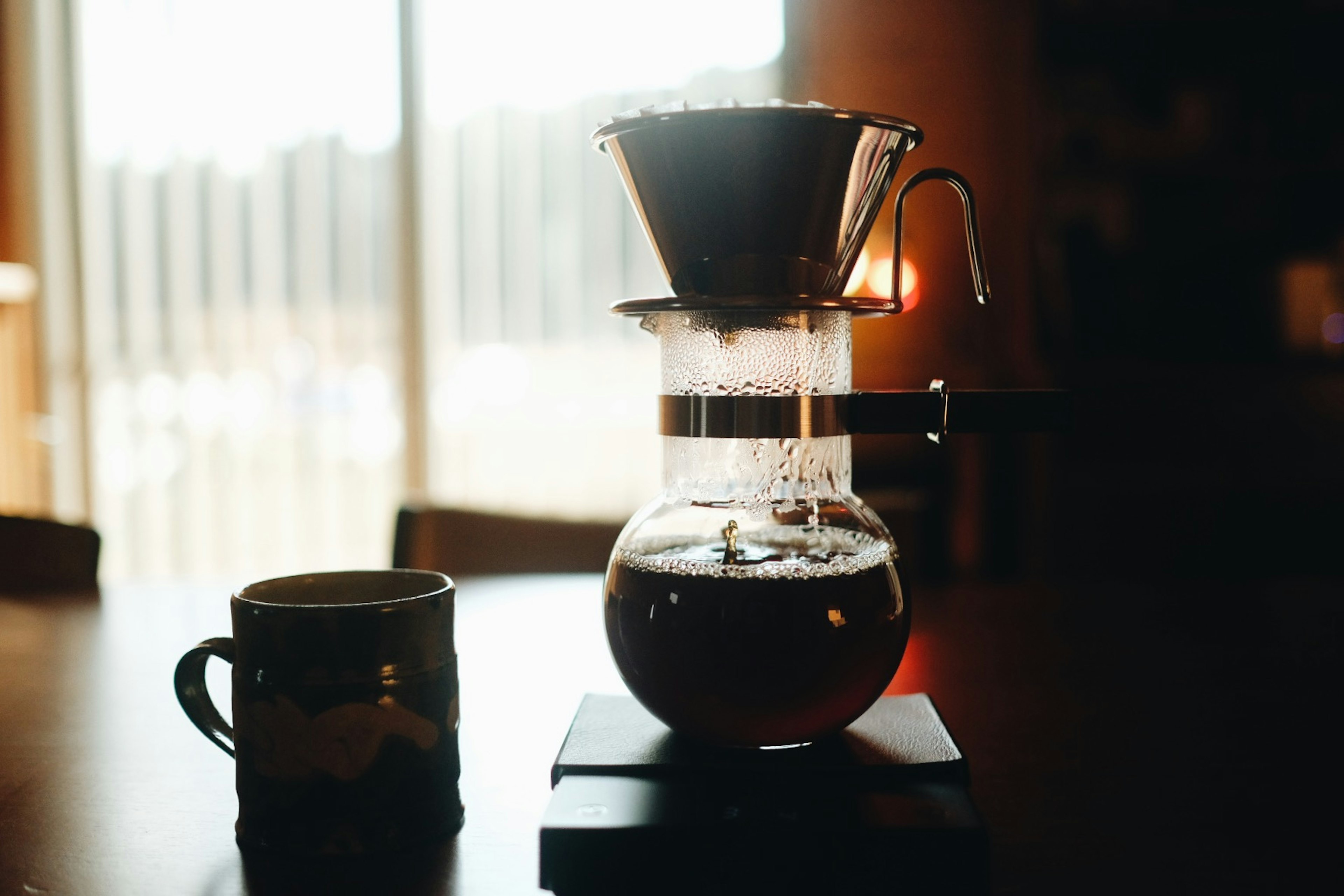 Filtrador de café con café preparado y una taza sobre una mesa