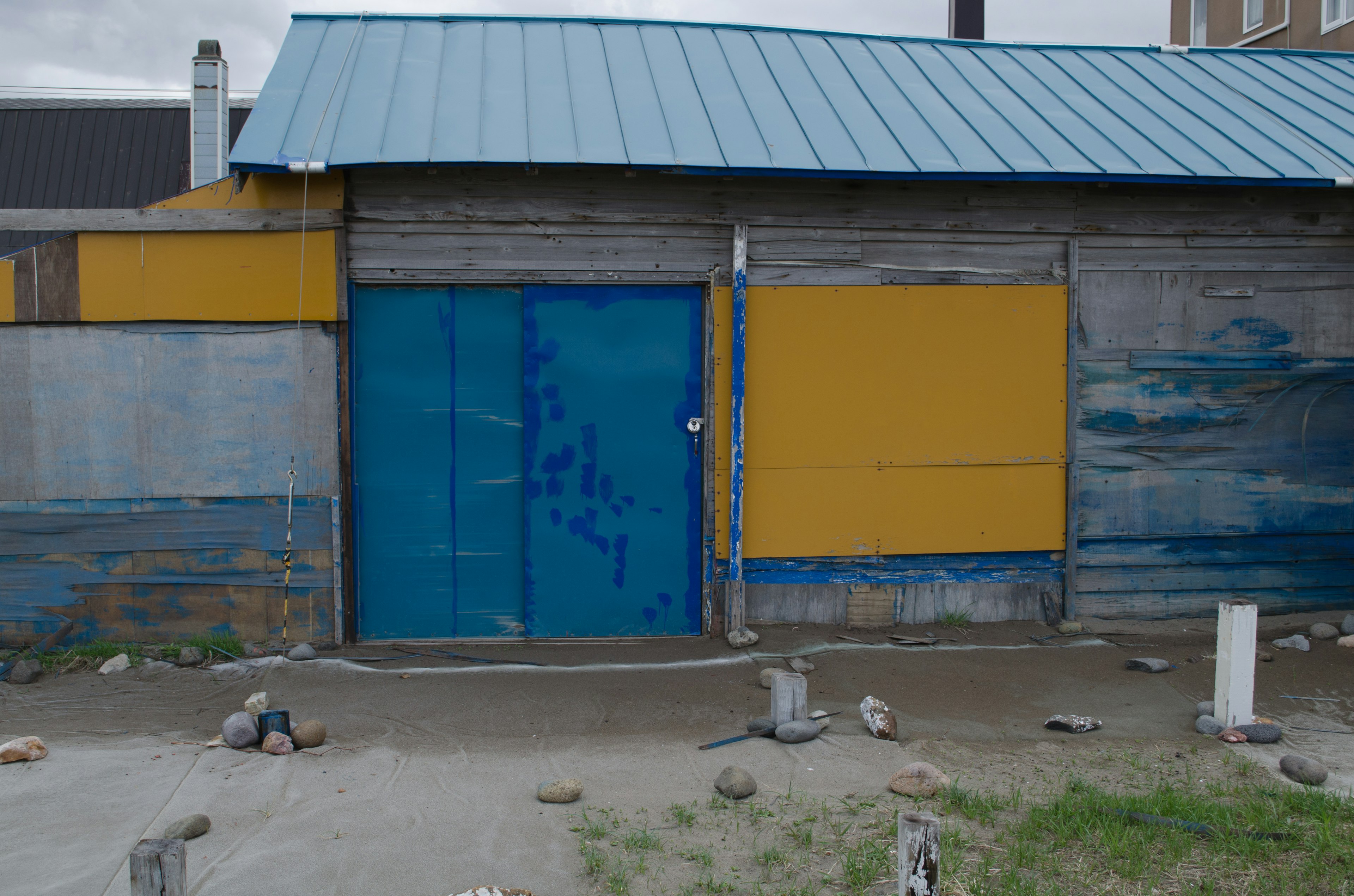 Exterior de un pequeño edificio con una puerta azul y una pared amarilla