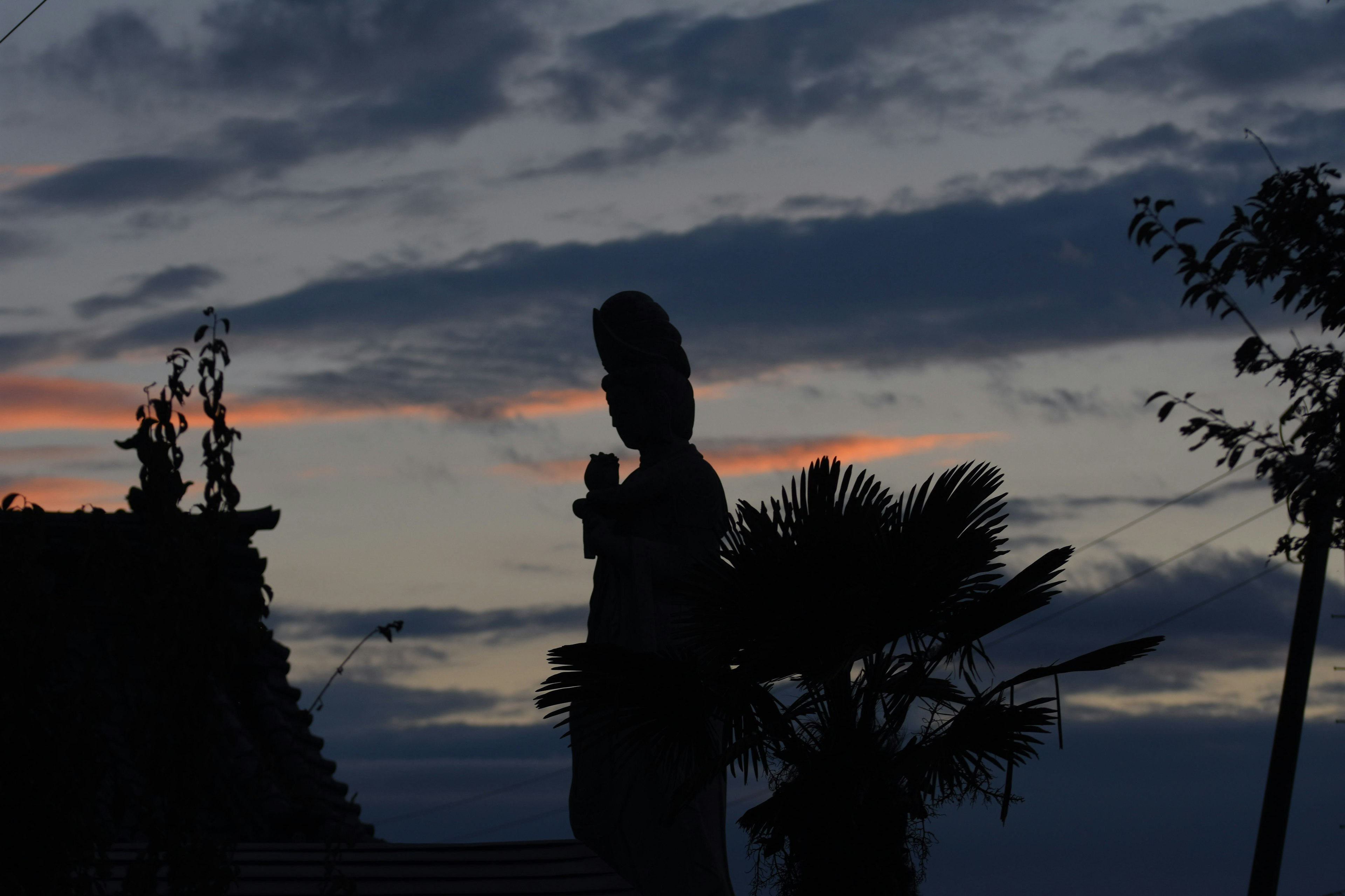 夕暮れの空にシルエットの神像が立っている