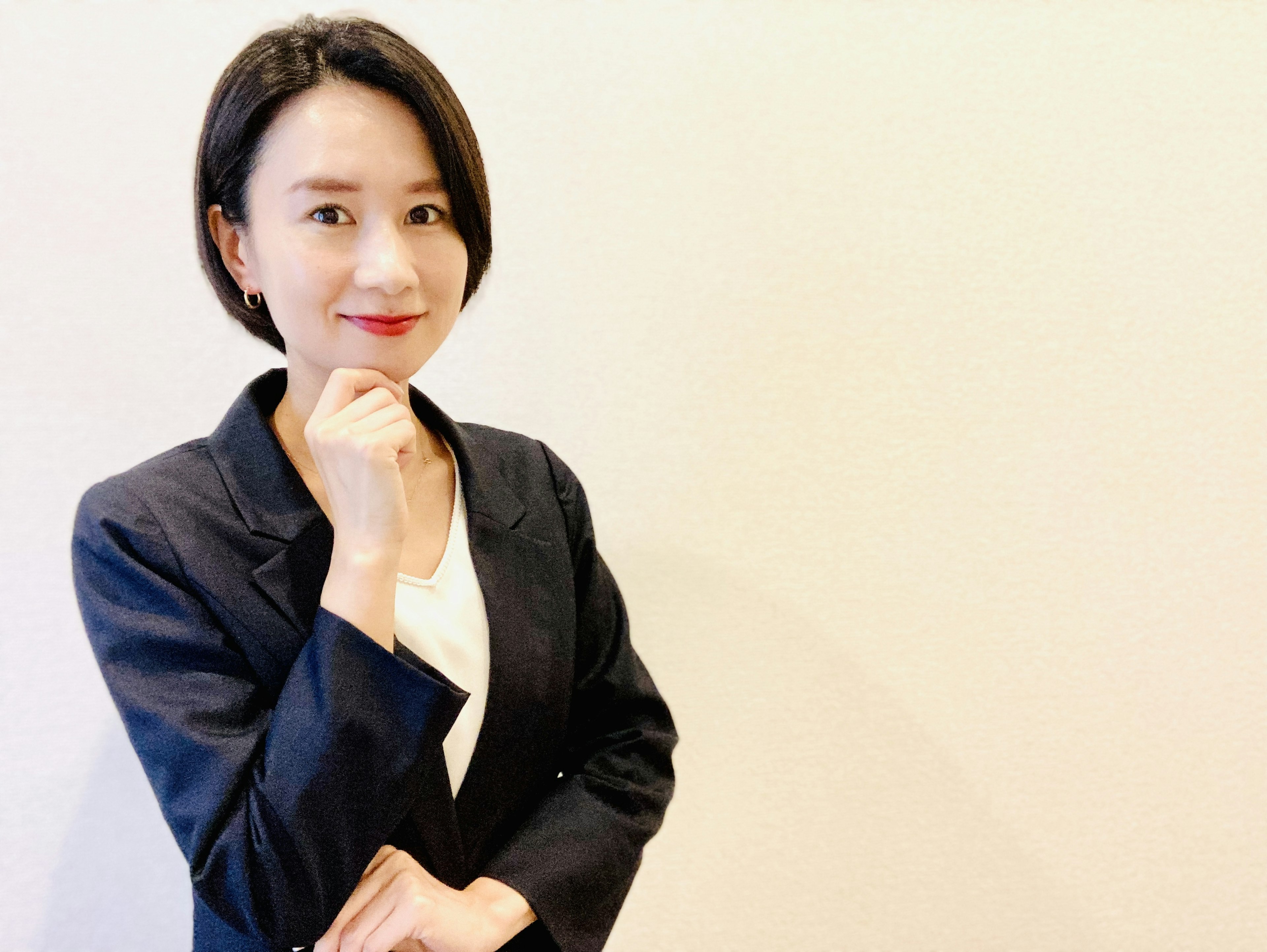 A woman in a business suit smiling with her hand on her chin