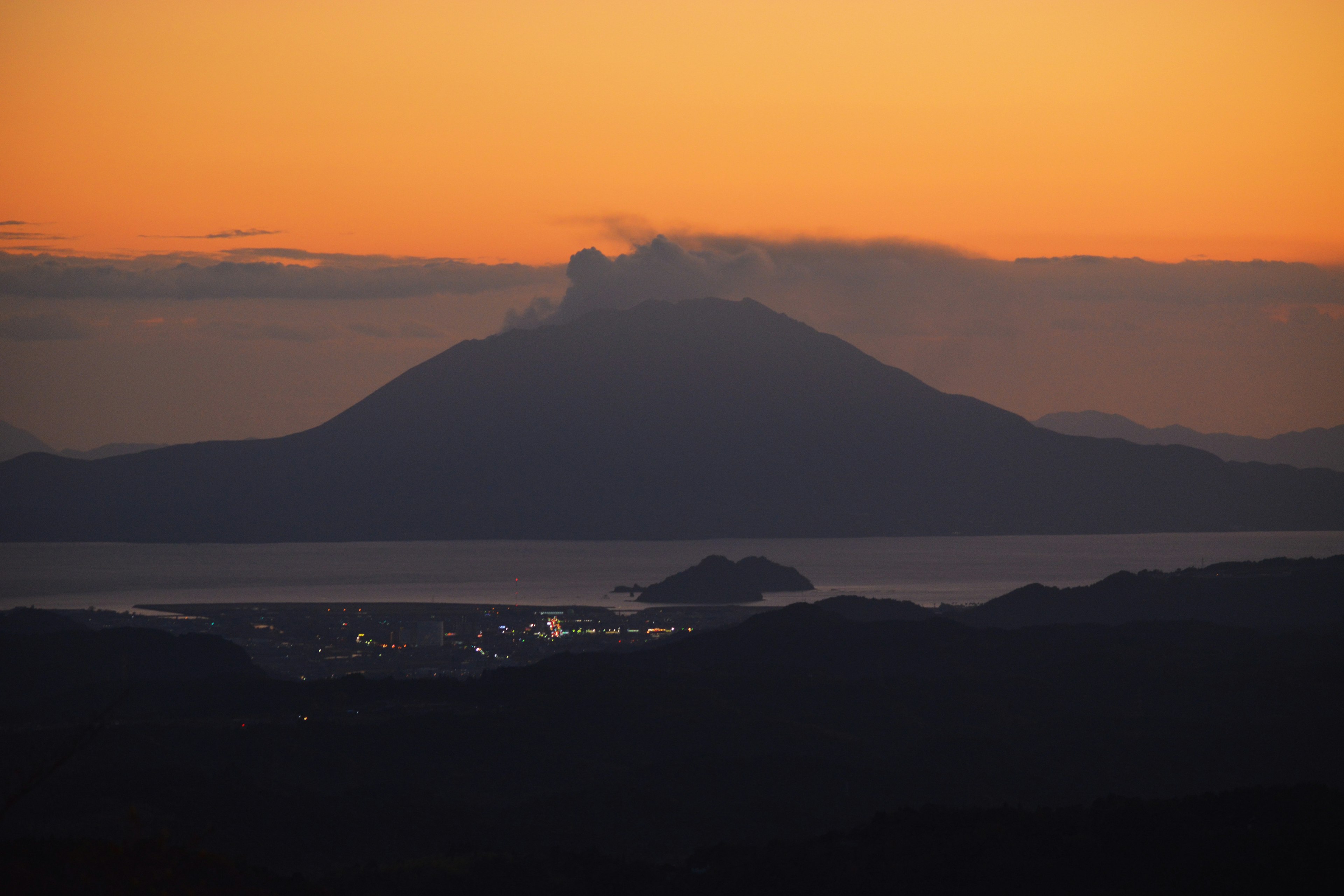 Silhouette eines Vulkans gegen einen Sonnenuntergang mit einer kleinen Insel im Vordergrund