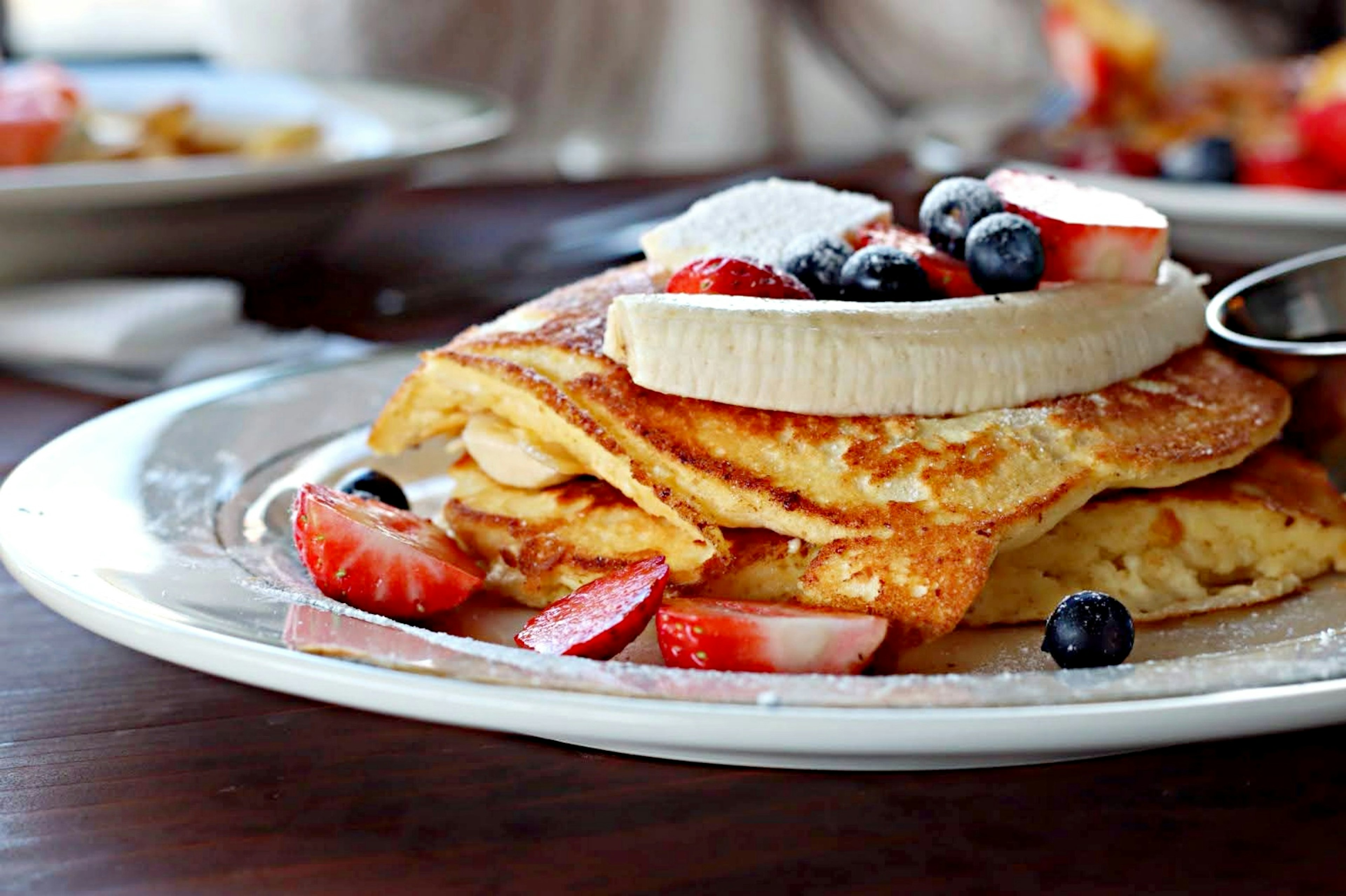 Pancakes esponjosos cubiertos con plátano, fresas y arándanos en un plato de desayuno