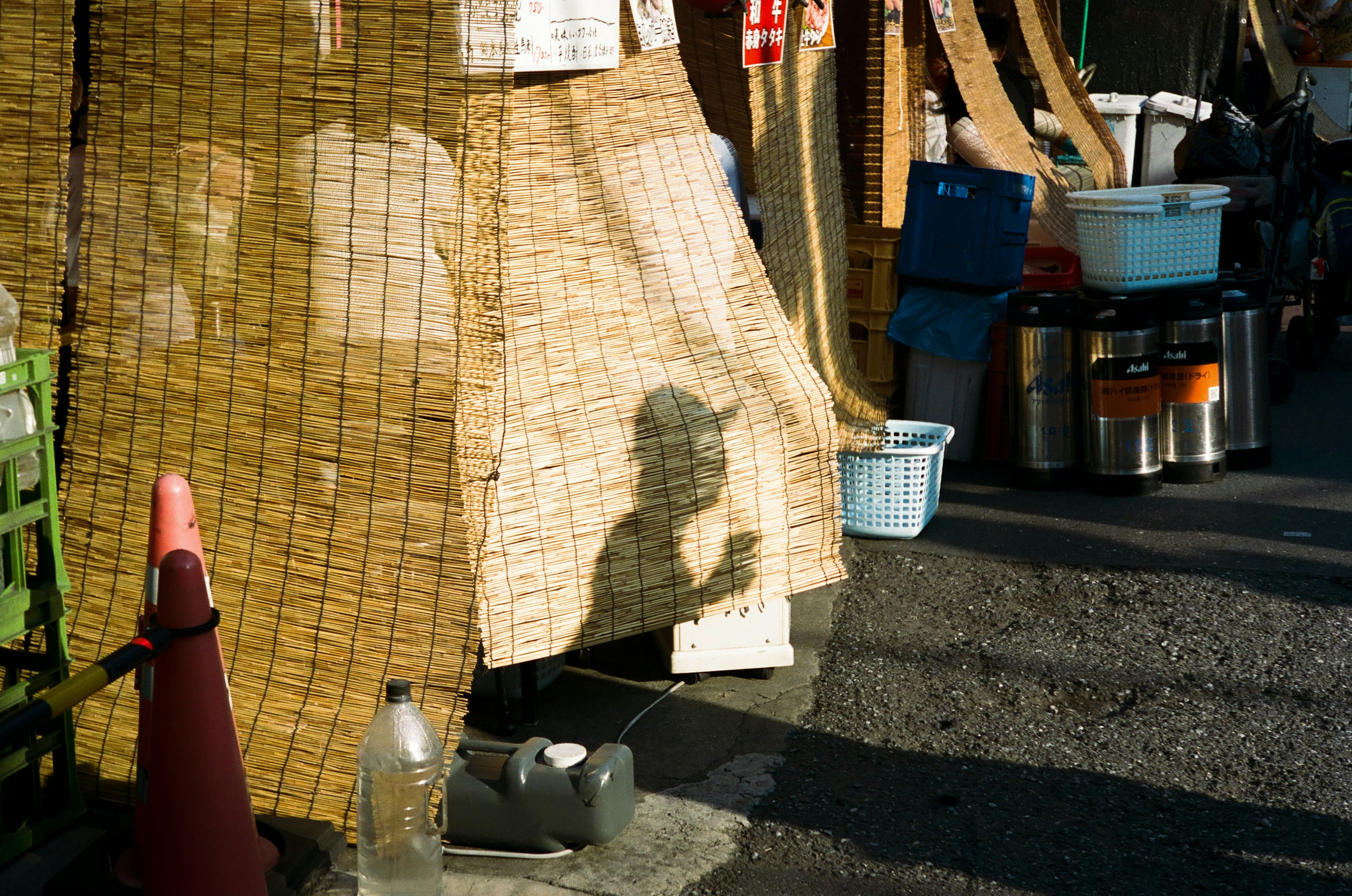 Market scene with a shadow cast on a bamboo screen various containers and a traffic cone