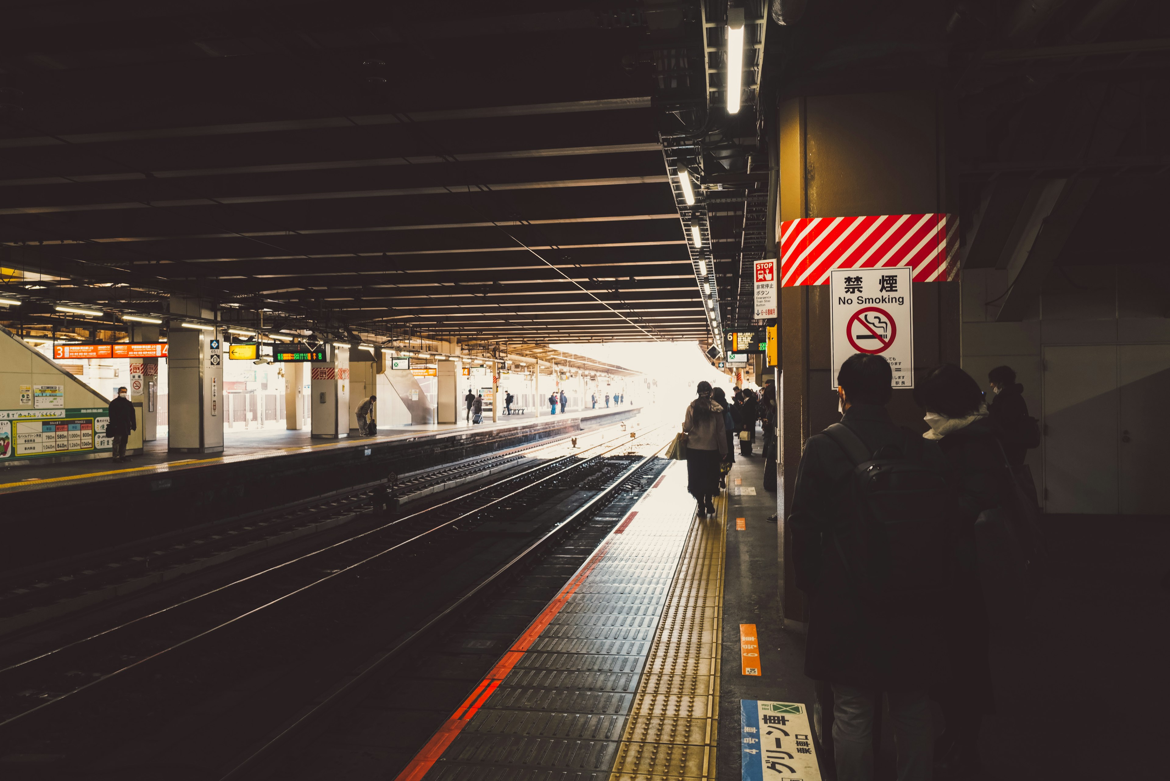 駅のプラットフォームで待つ人々と明るい光が見える