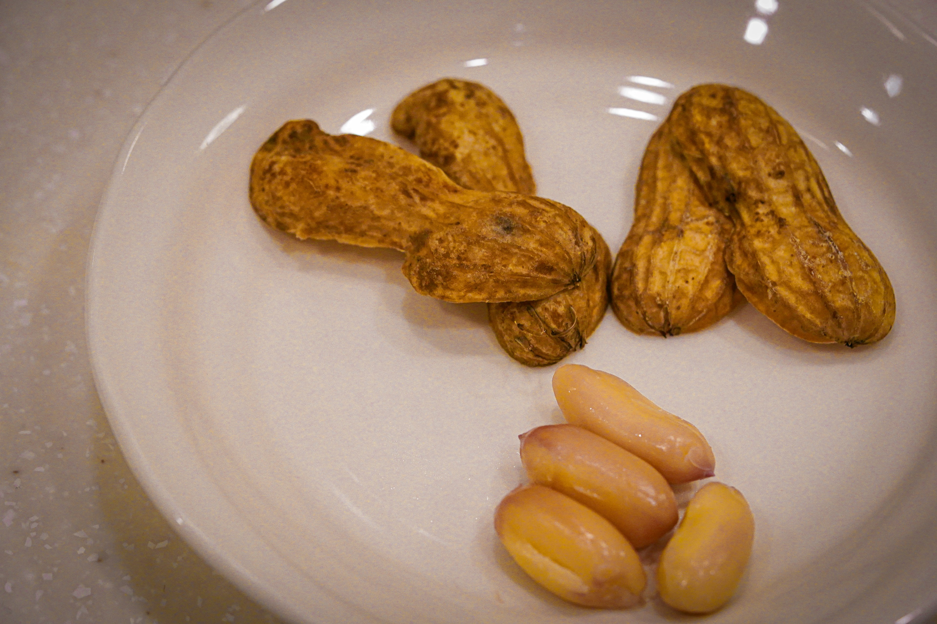 Kacang tanah dan kacang tanah yang sudah dikupas di atas piring