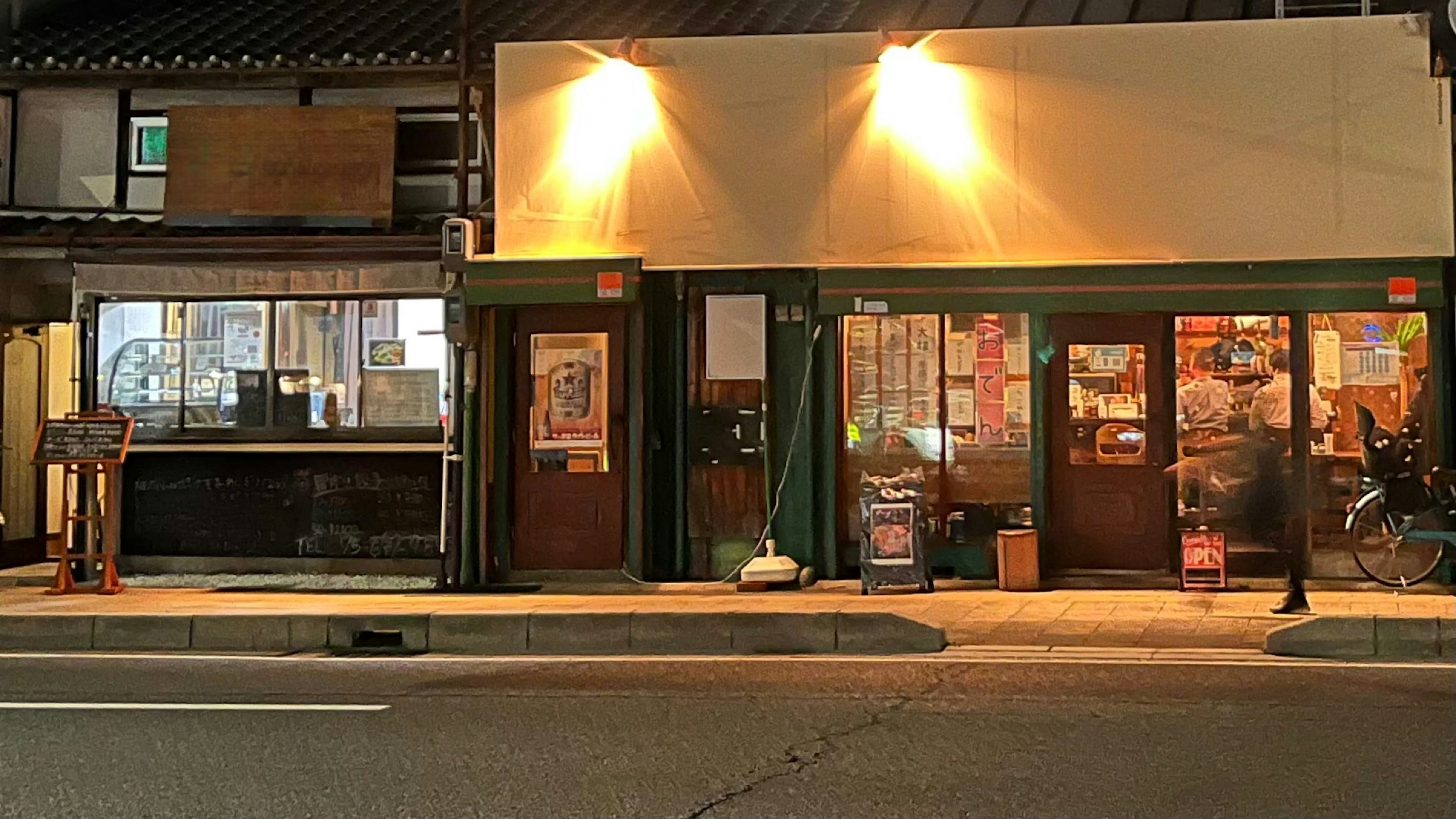 Una tienda con exterior verde y luces brillantes en una calle comercial nocturna