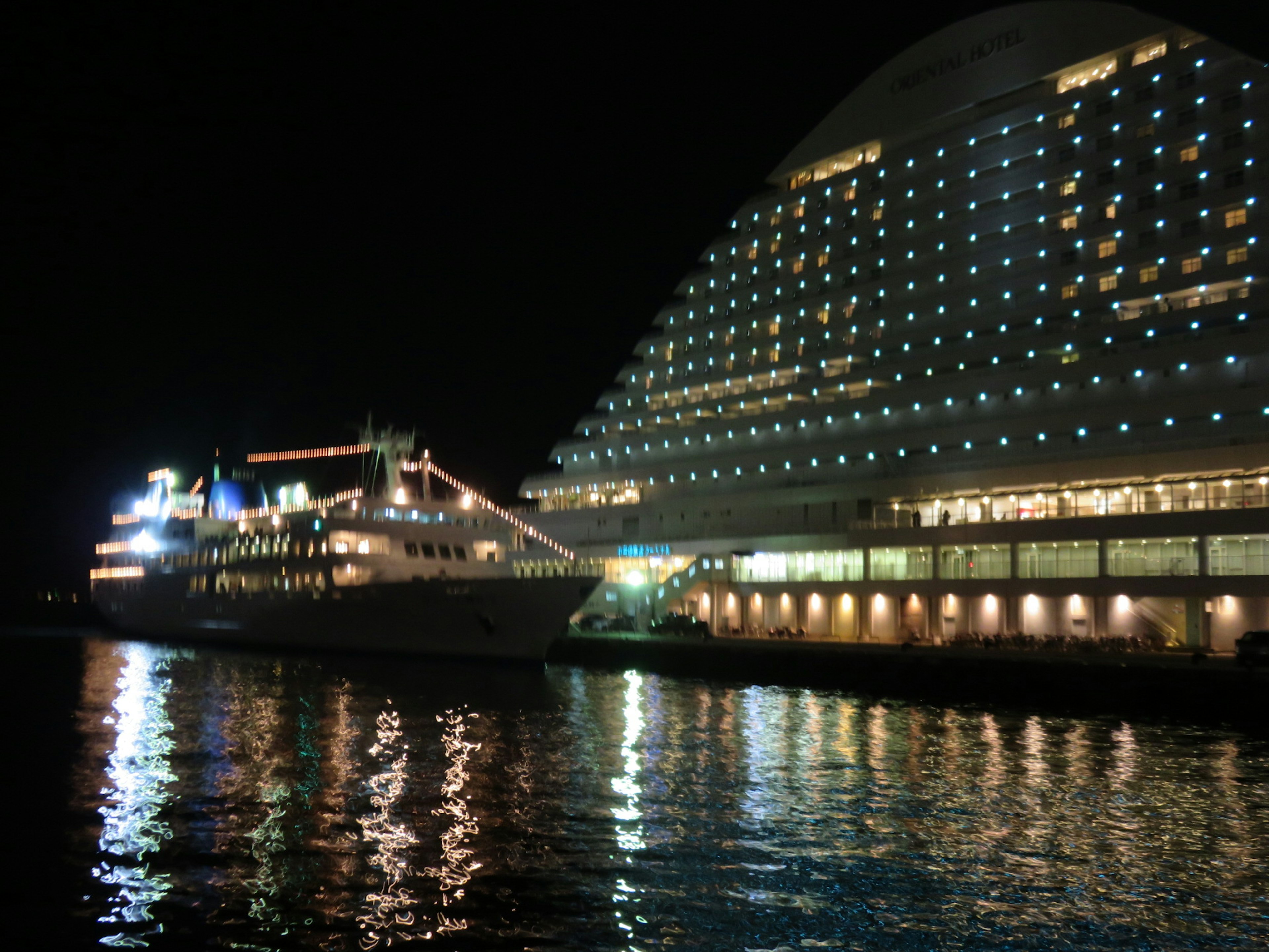 Navire de croisière luxueux amarré la nuit à côté d'un bâtiment magnifiquement éclairé