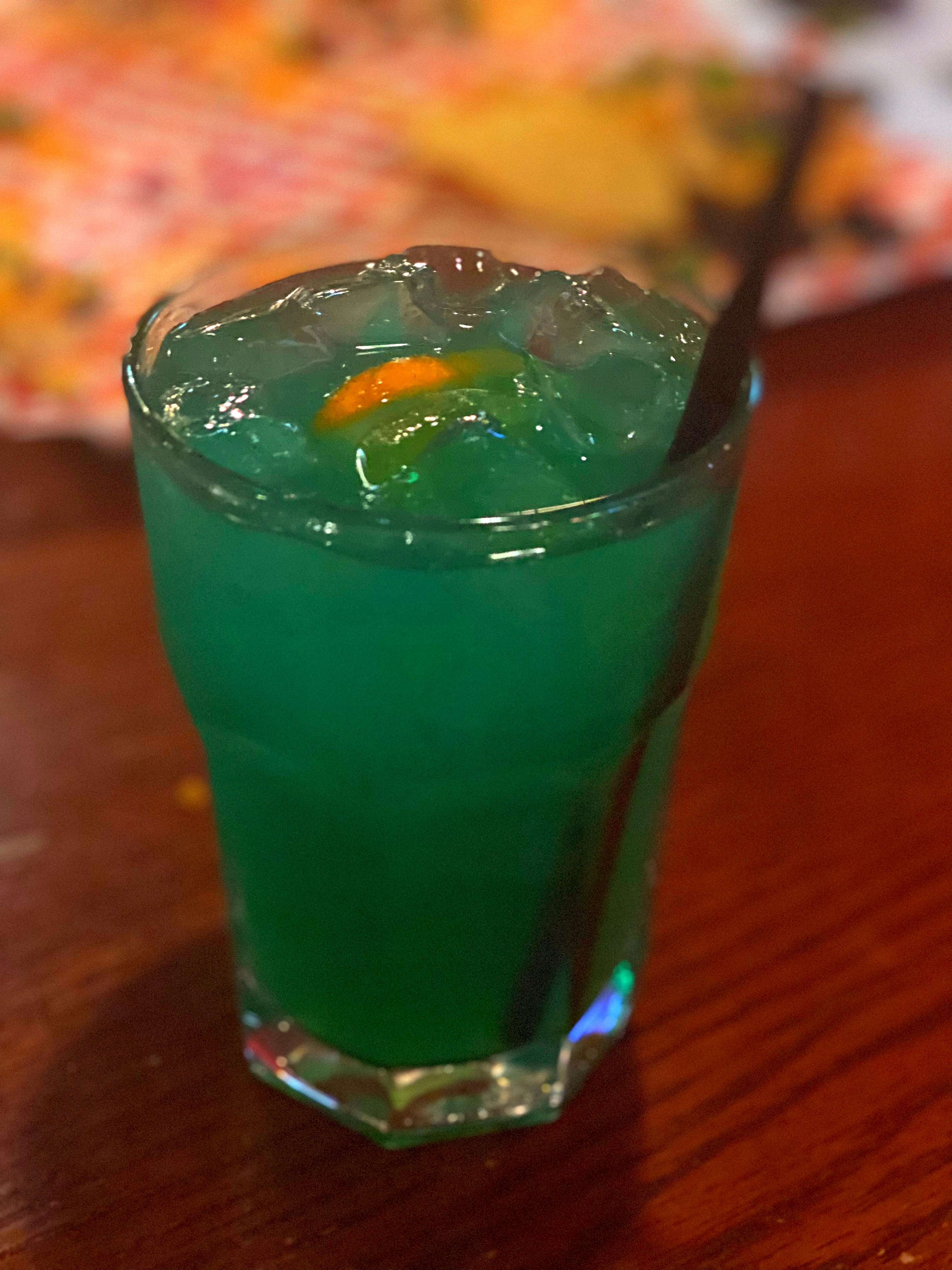 A blue cocktail with ice and an orange slice on top