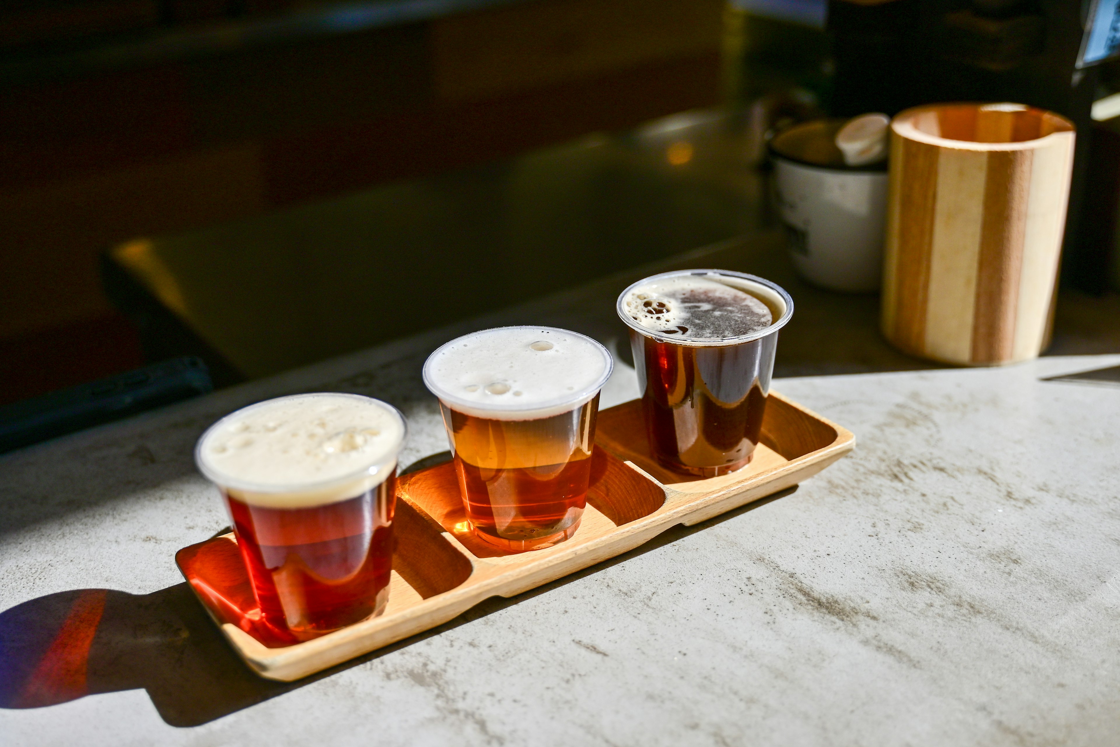 Three beer samples in clear cups on a wooden tray