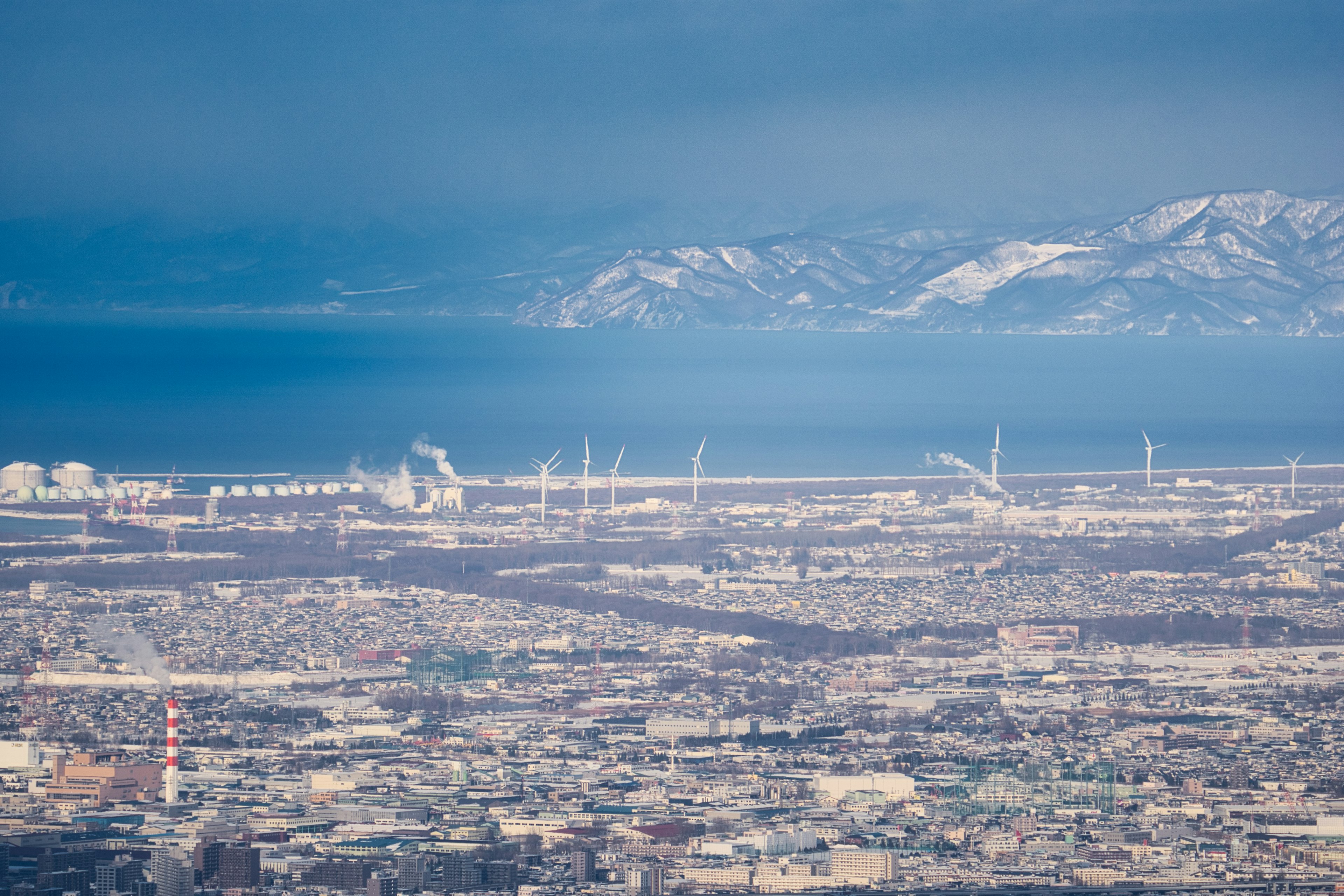 Städtische Landschaft mit Windkraftanlagen Bergen und Meer im Hintergrund