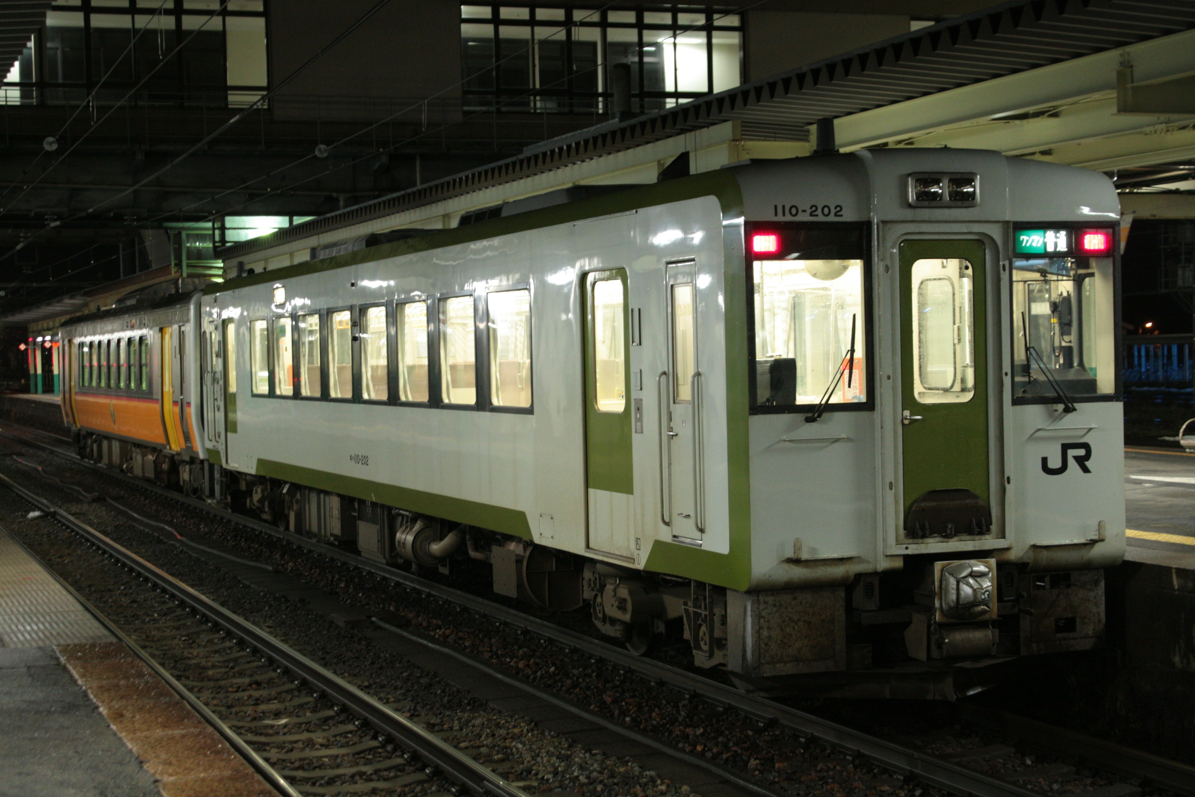 夜の駅で停車中のJRの列車 蛍光灯の明かりが車両を照らす