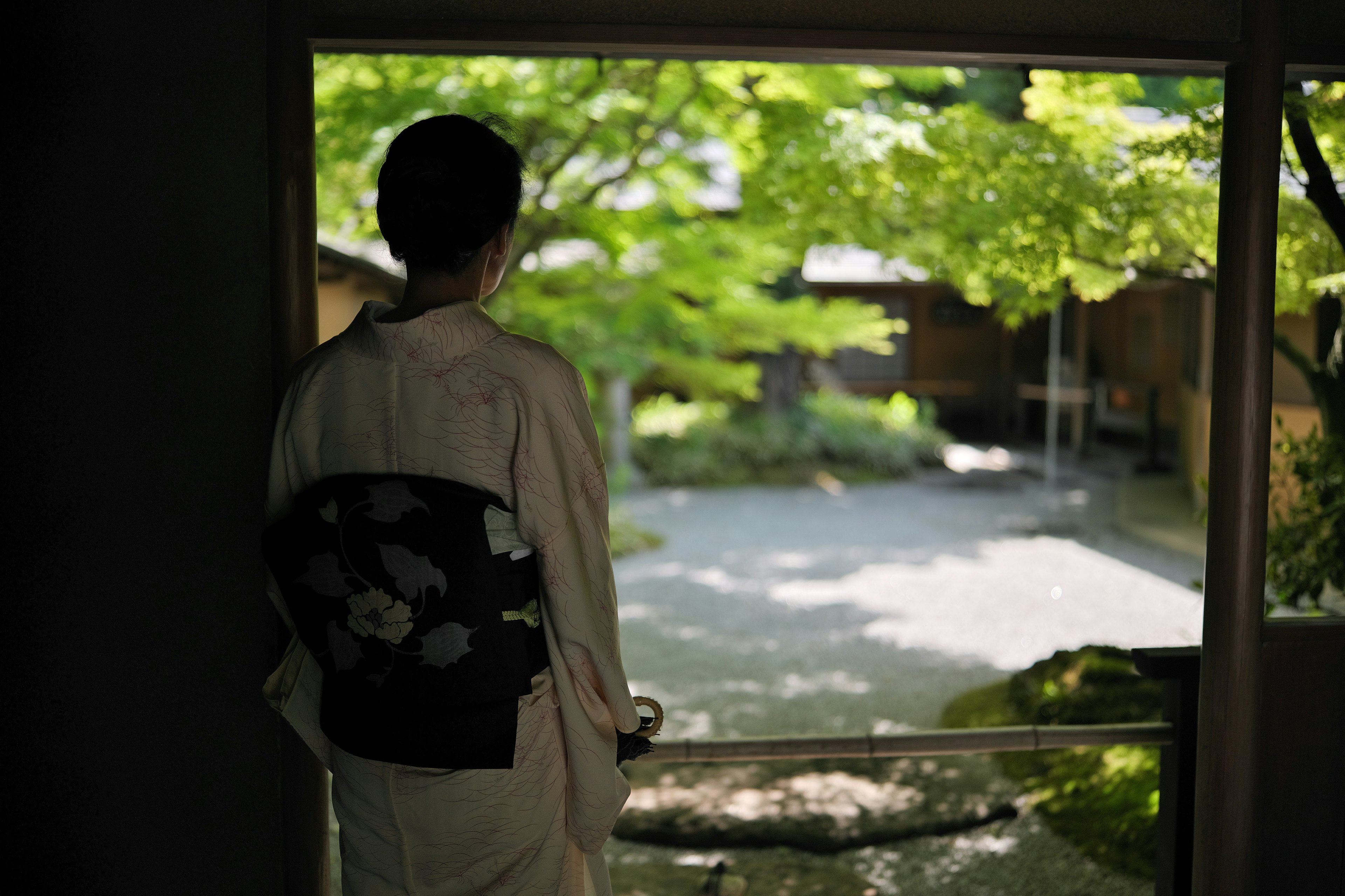 和服を着た人物が庭を眺めているシーン 緑の木々と静かな空間が広がる