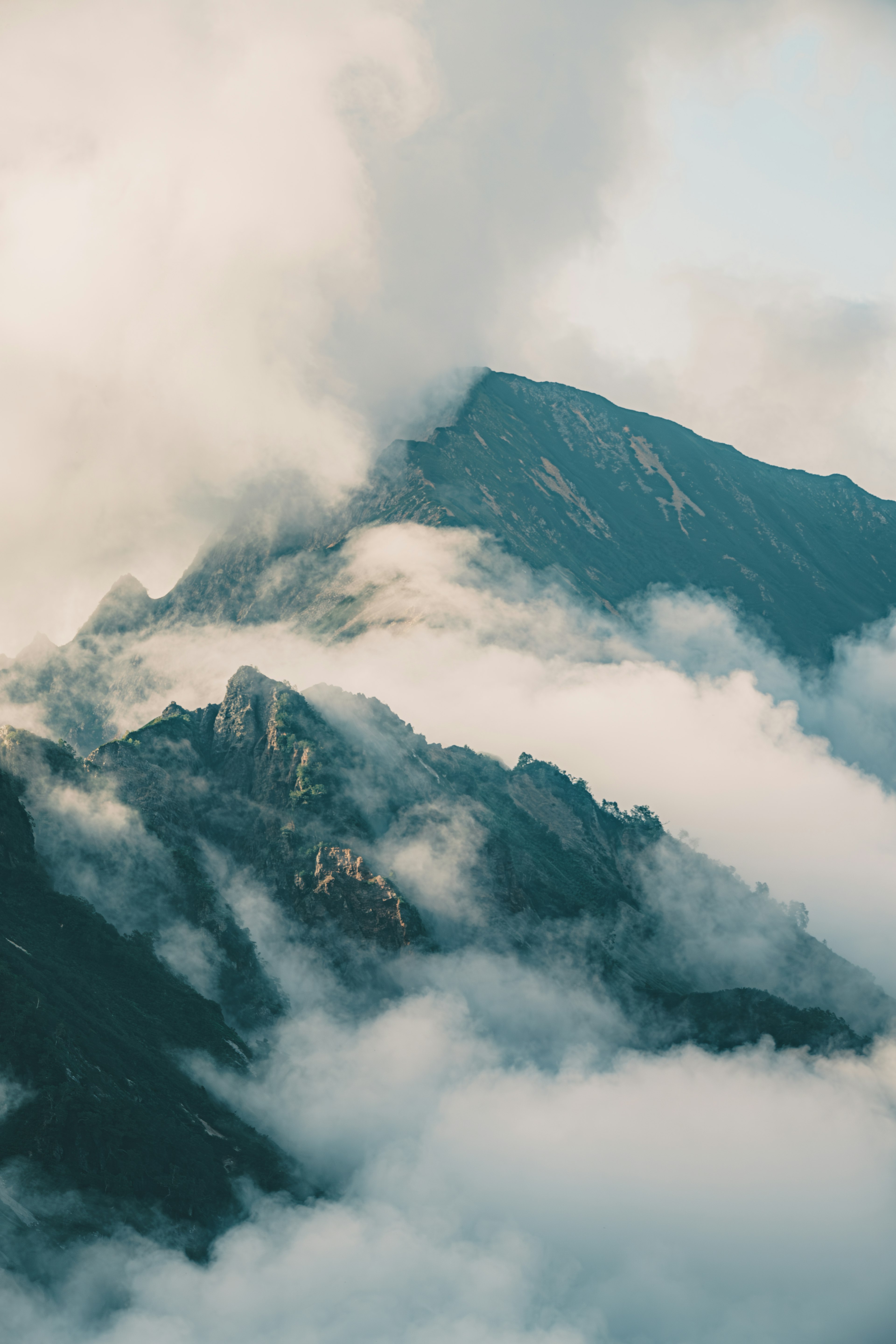 Paysage montagneux couvert de nuages avec de la brume s'élevant du sommet créant une atmosphère mystique