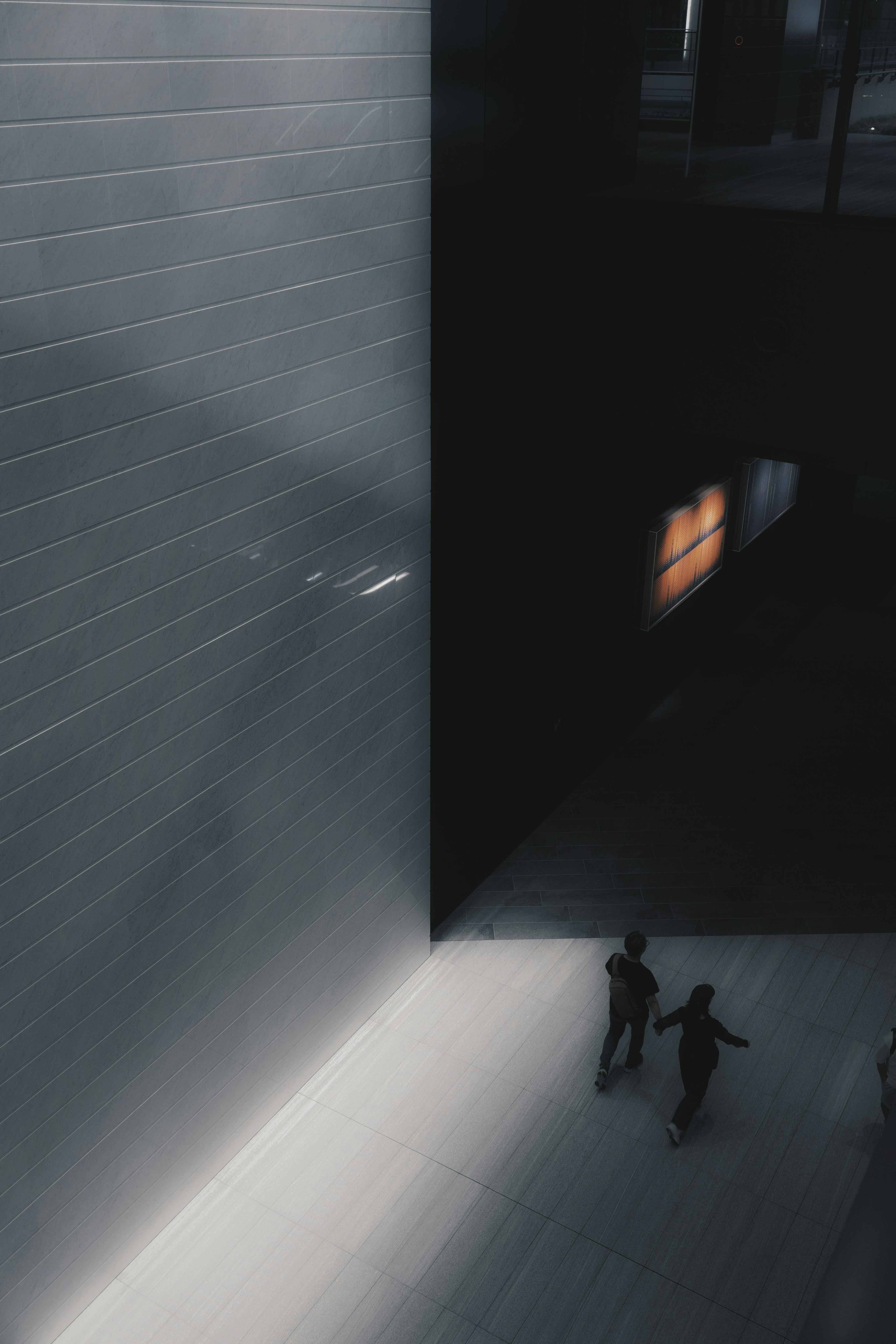 Deux silhouettes dans un espace sombre avec un mur lumineux