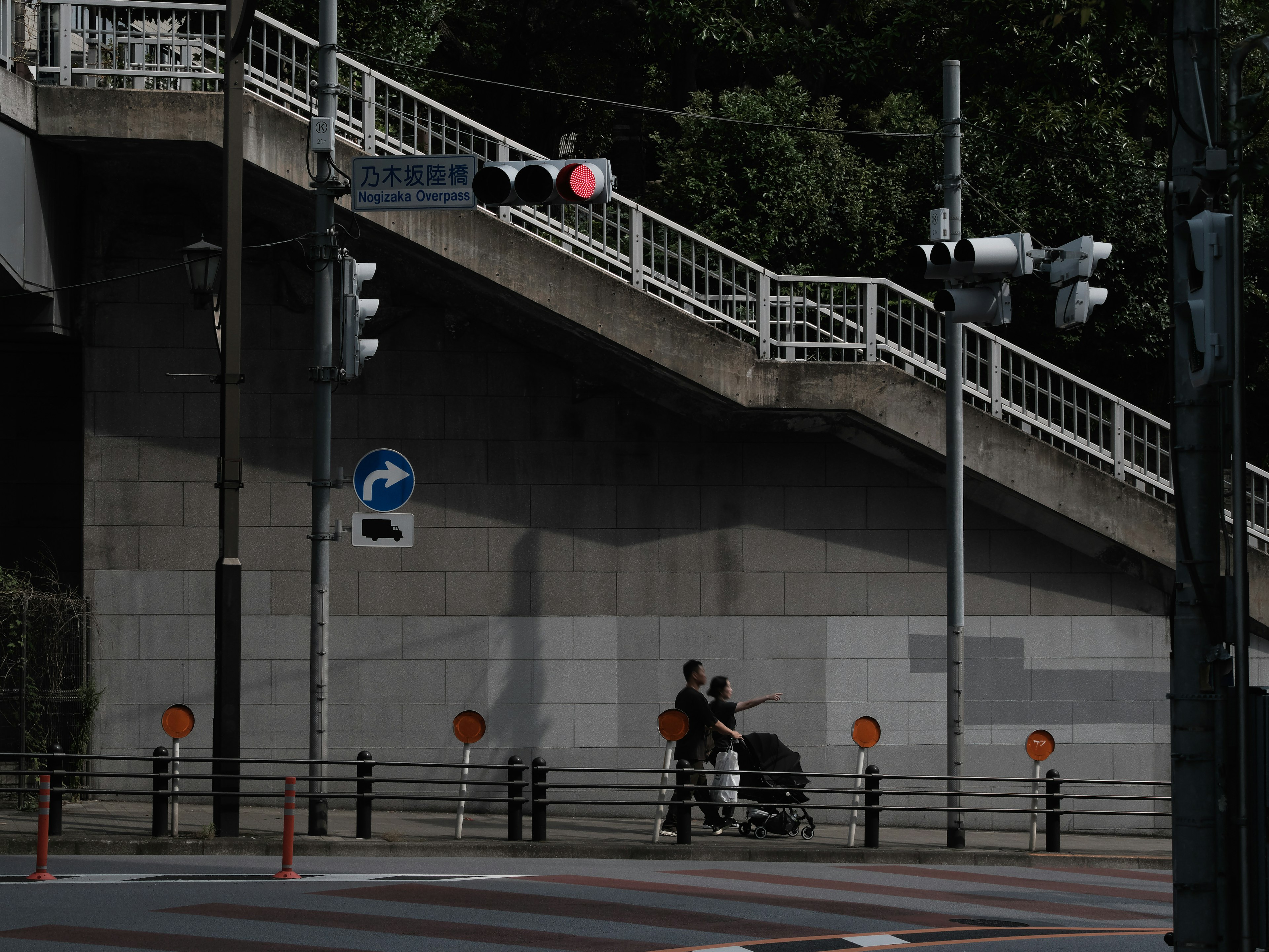 A person pushing a stroller under a traffic light with a red signal and stairs in the background