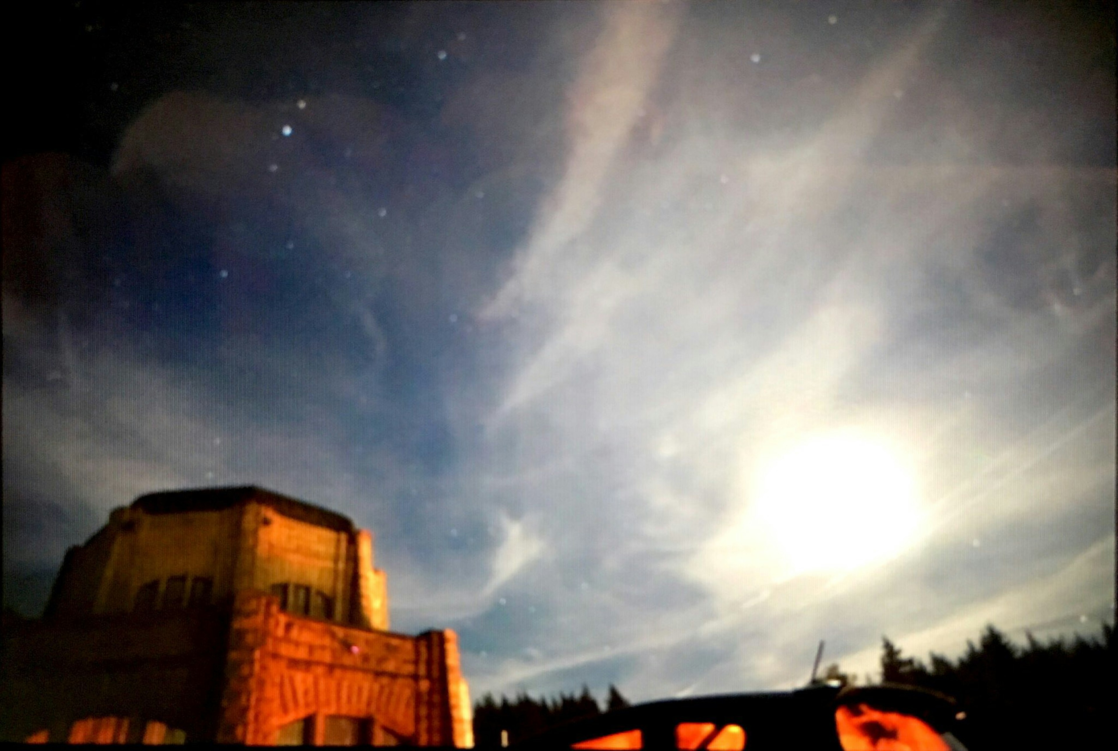 夜空に浮かぶ雲と星々と月を背景にした建物のシルエット