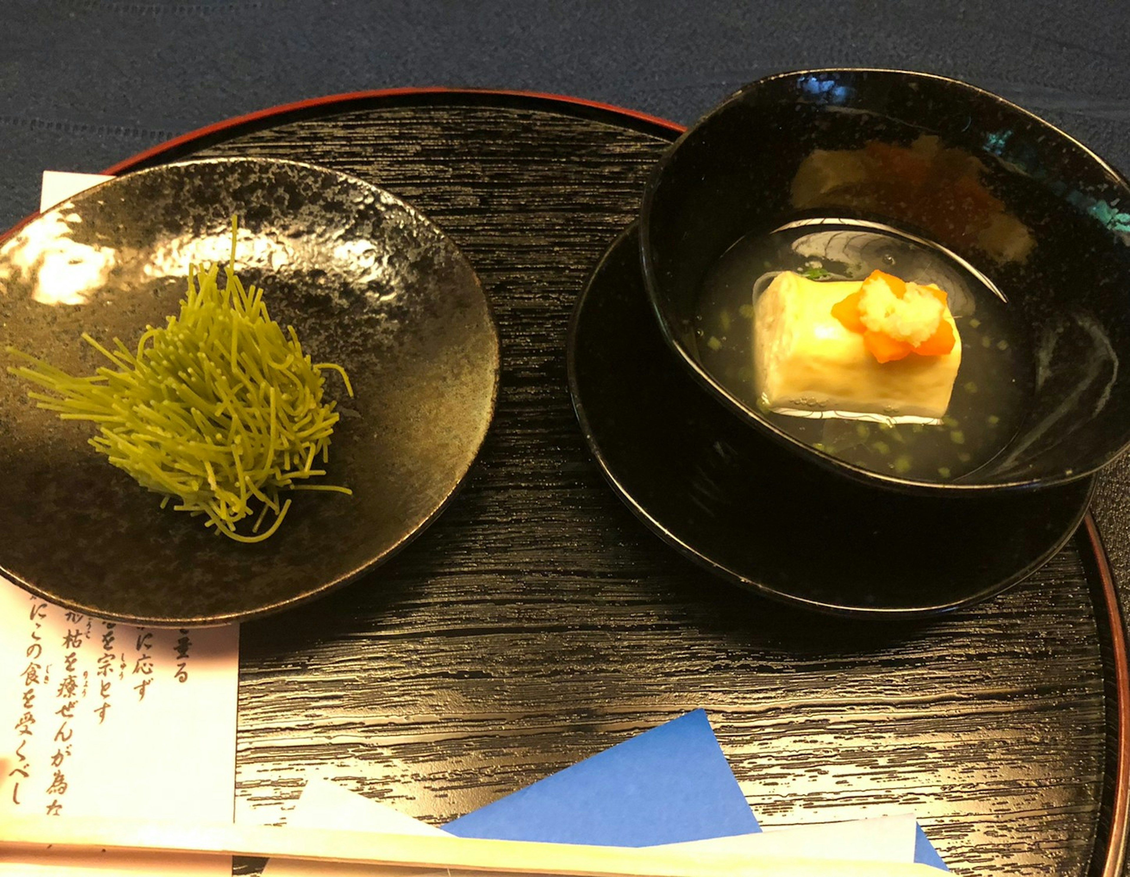 Plat noir avec algues vertes et un bol de tofu dans un bouillon clair