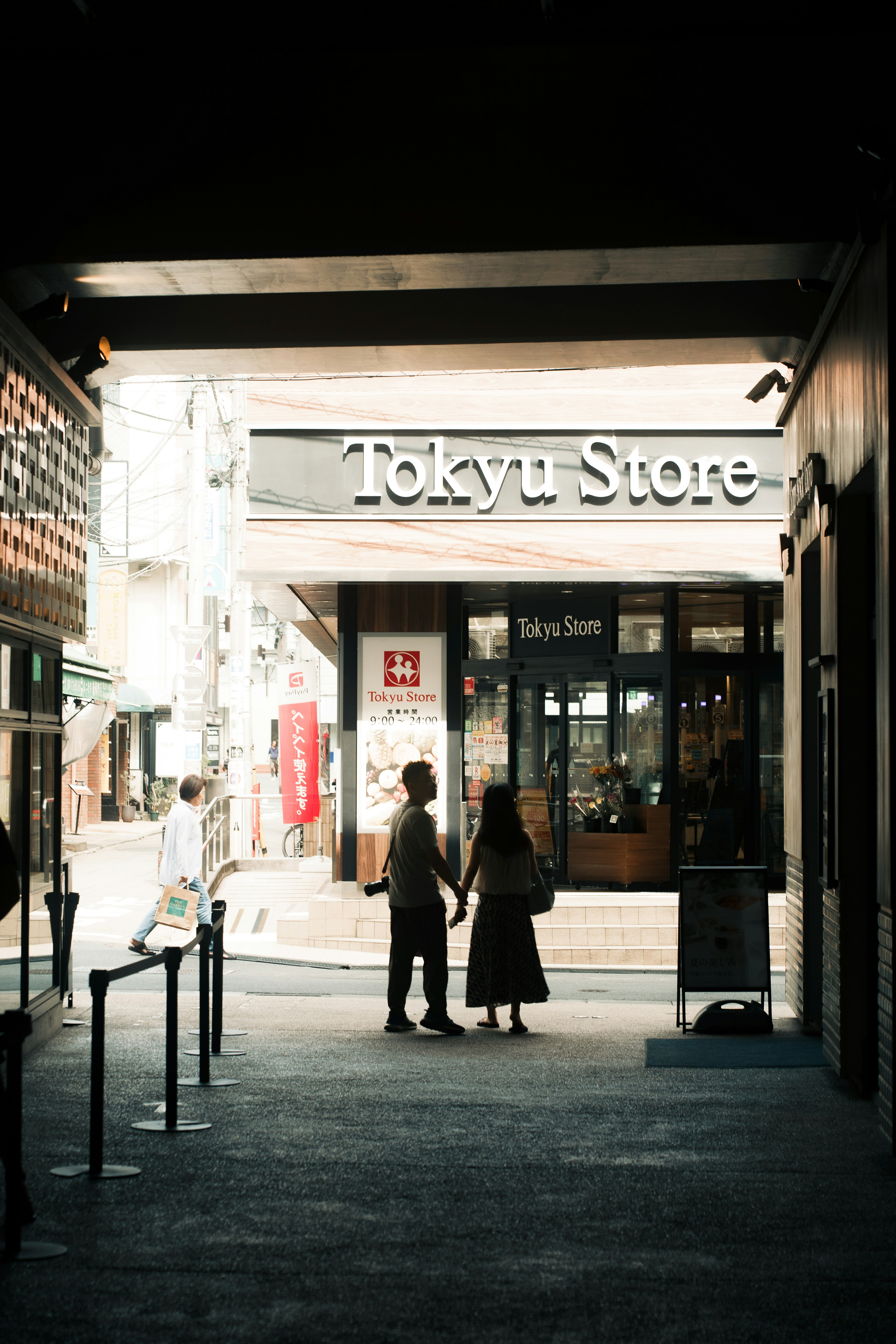 Silhouette of a couple holding hands in front of Tokyu Store