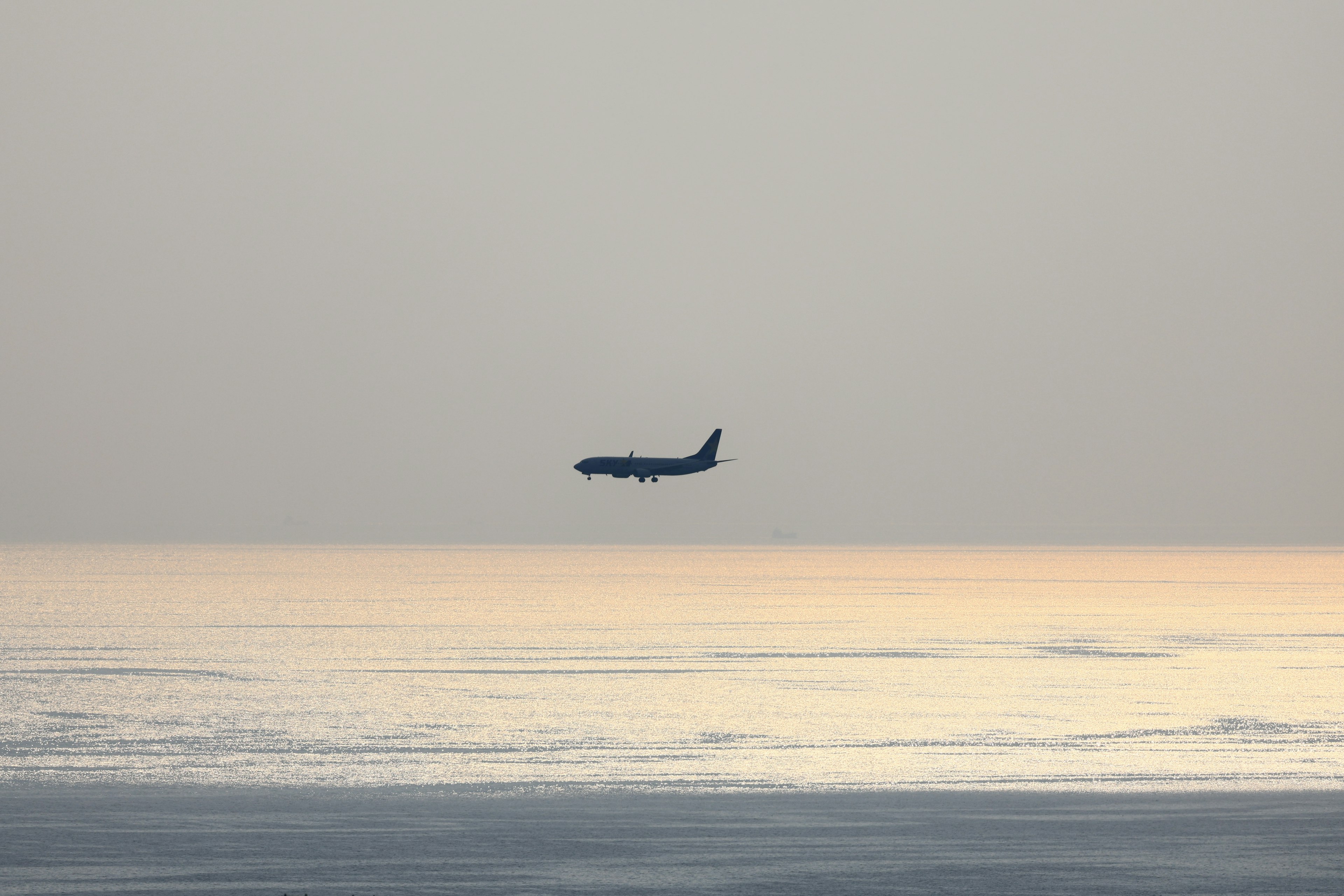 海上を飛行中の航空機のシルエットが薄明かりの中に浮かぶ