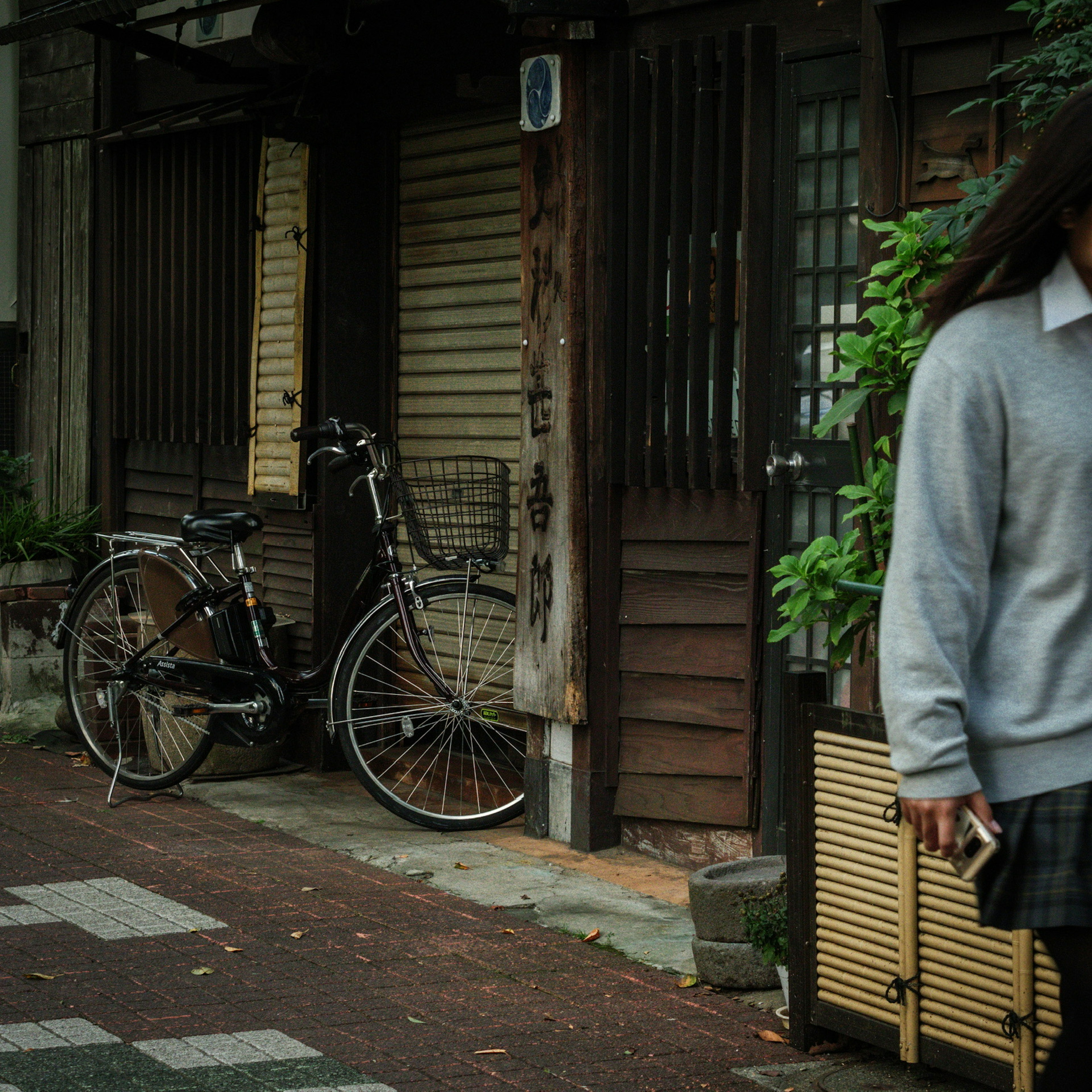 Una chica con uniforme escolar caminando junto a una calle vintage con una bicicleta