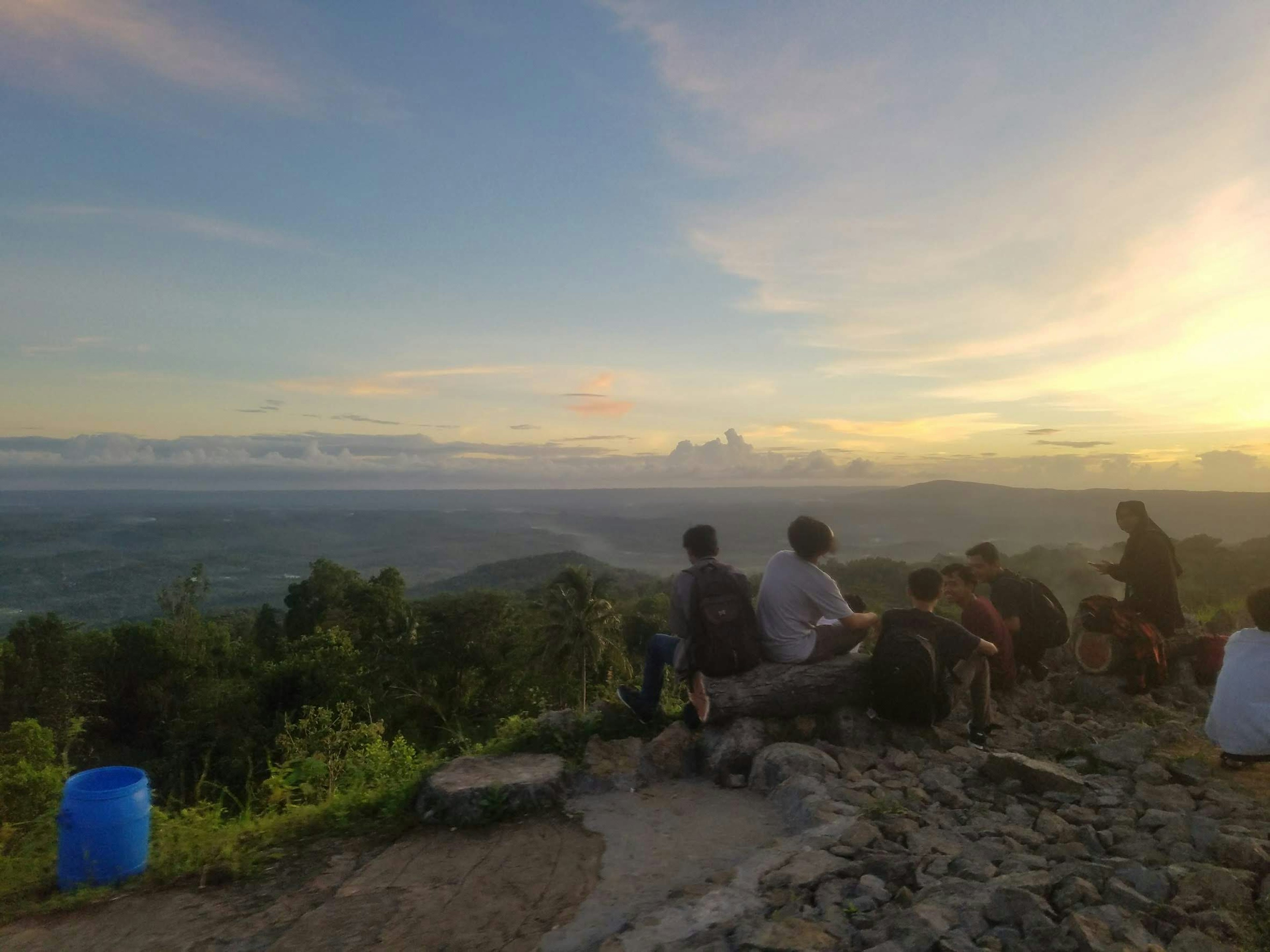 Silhouette di persone sedute in cima a una montagna al tramonto con un bel paesaggio