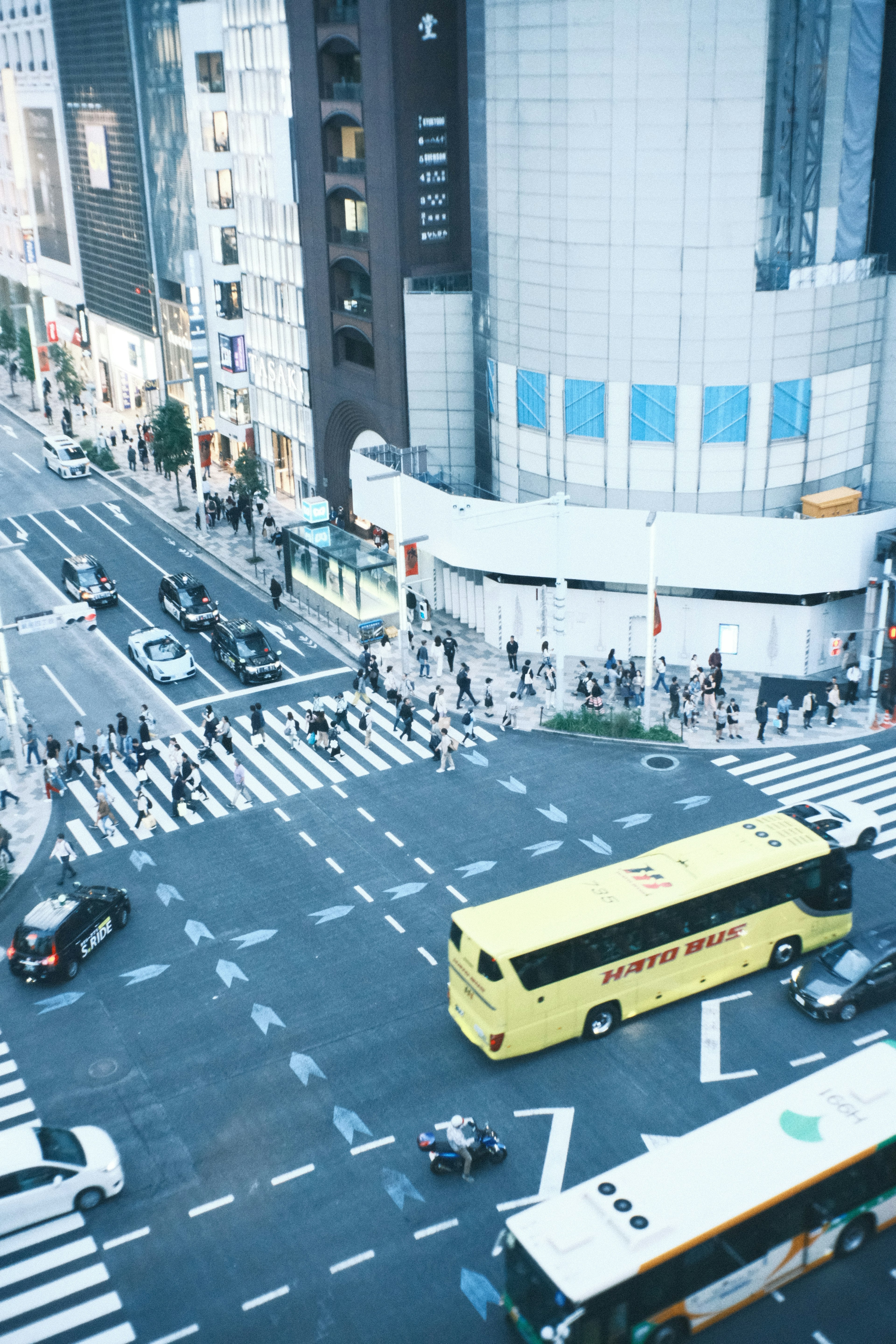 渋谷の交差点の上からの眺めで、黄色のバスと多くの人々が行き交う様子