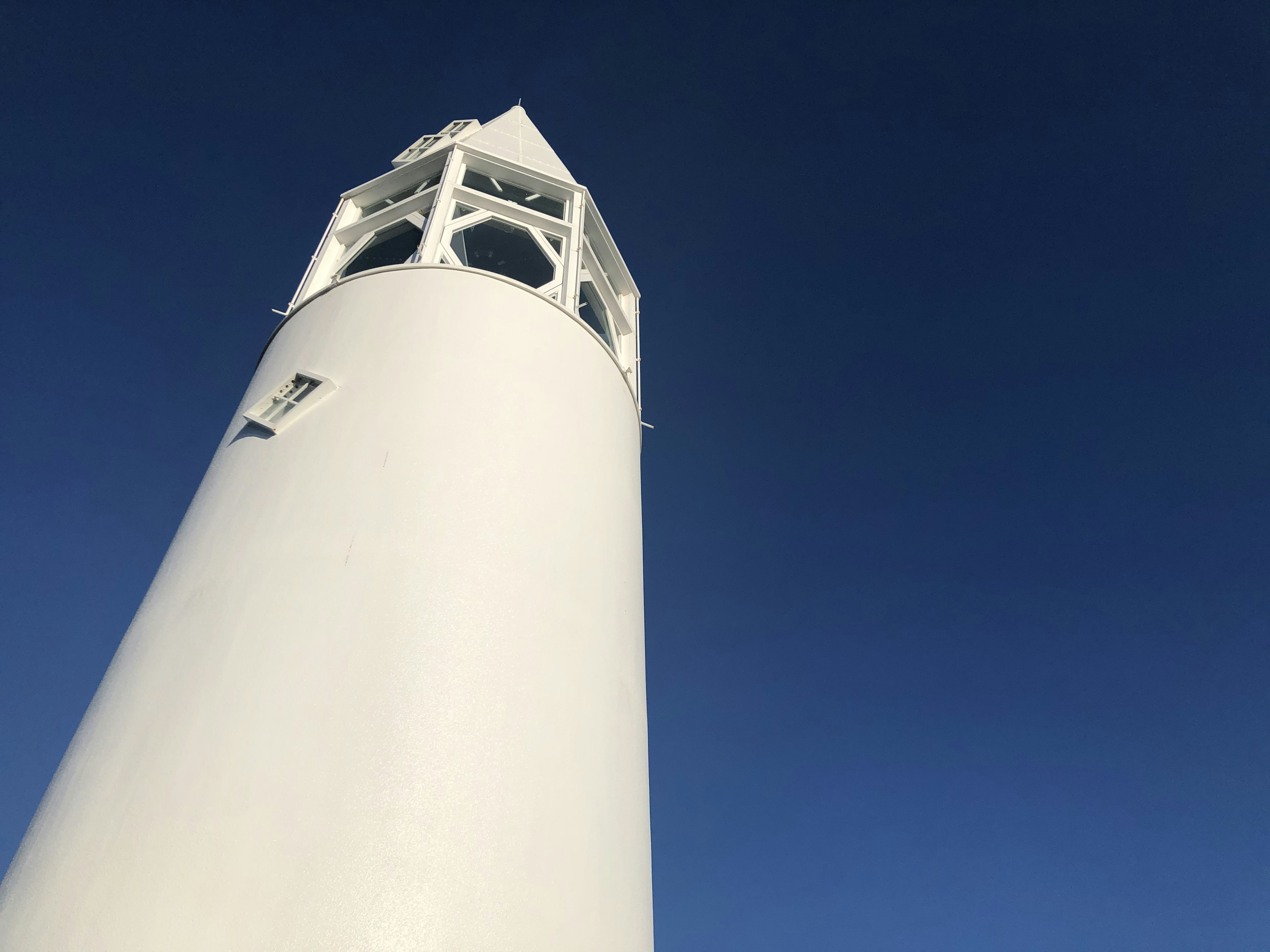 Close-up of a white lighthouse towering under a blue sky