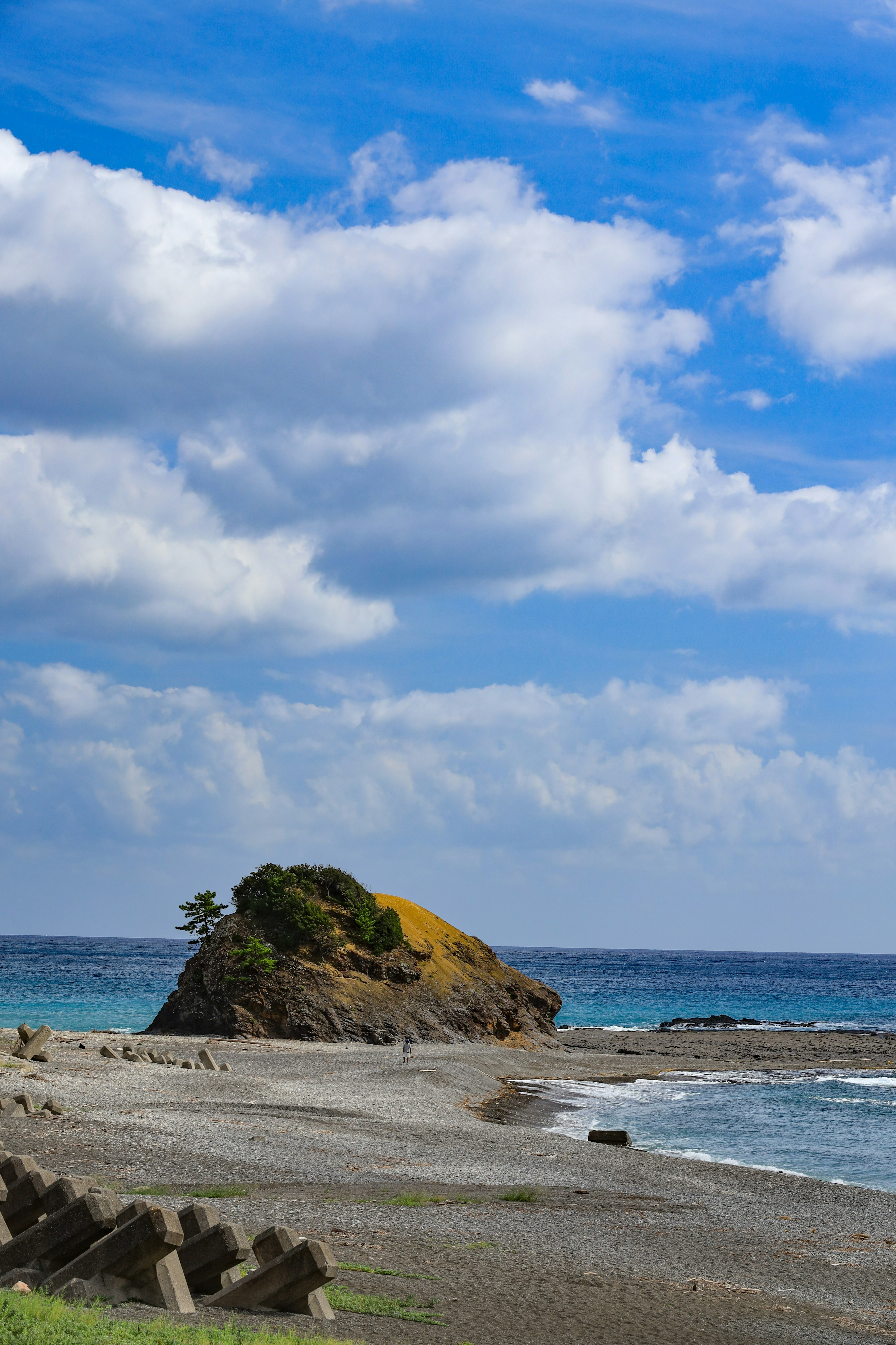 Pemandangan pantai dengan pulau berbatu di bawah langit biru dan awan