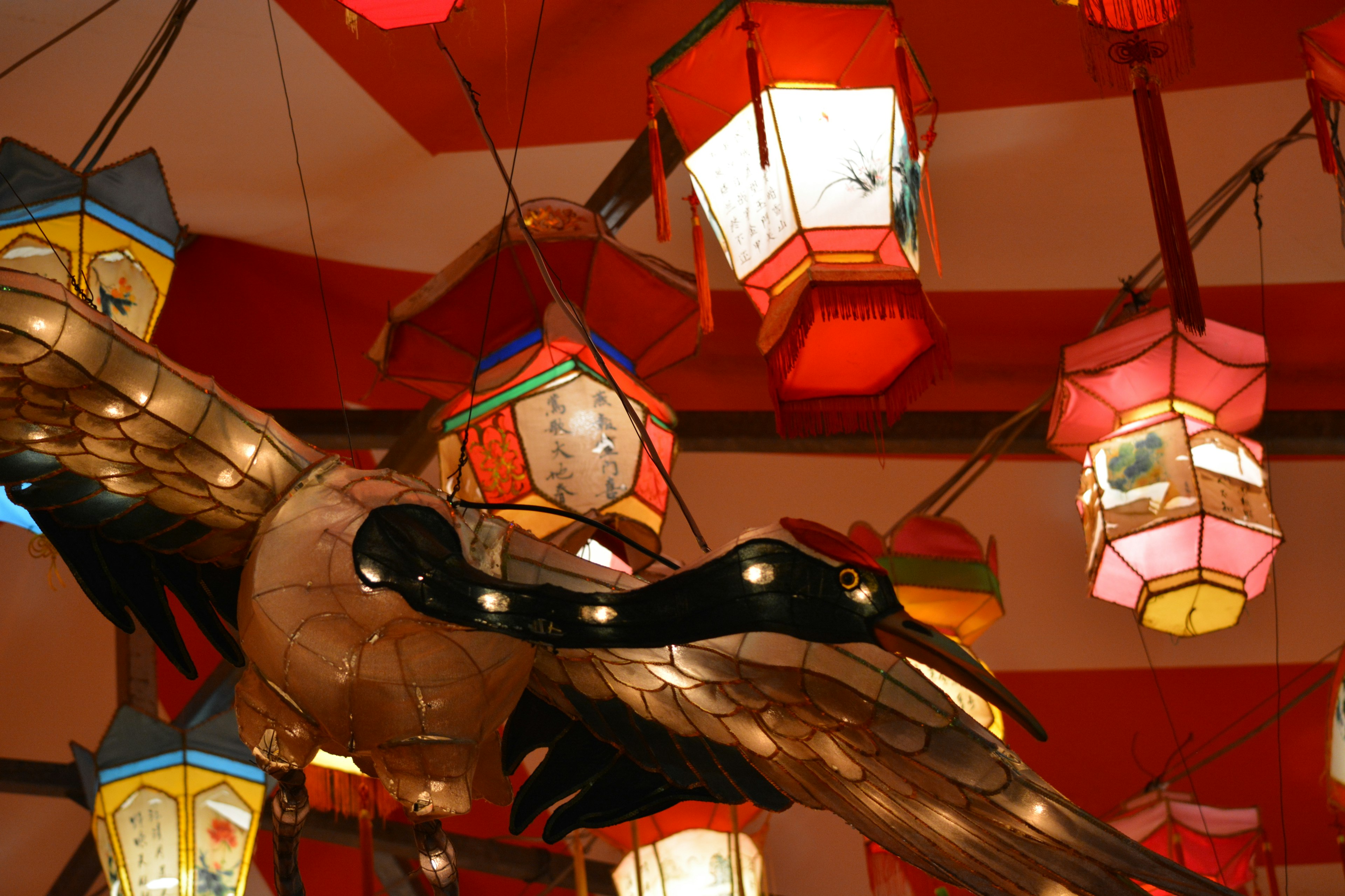 Colorful lanterns hanging from a red ceiling with a wooden bird sculpture