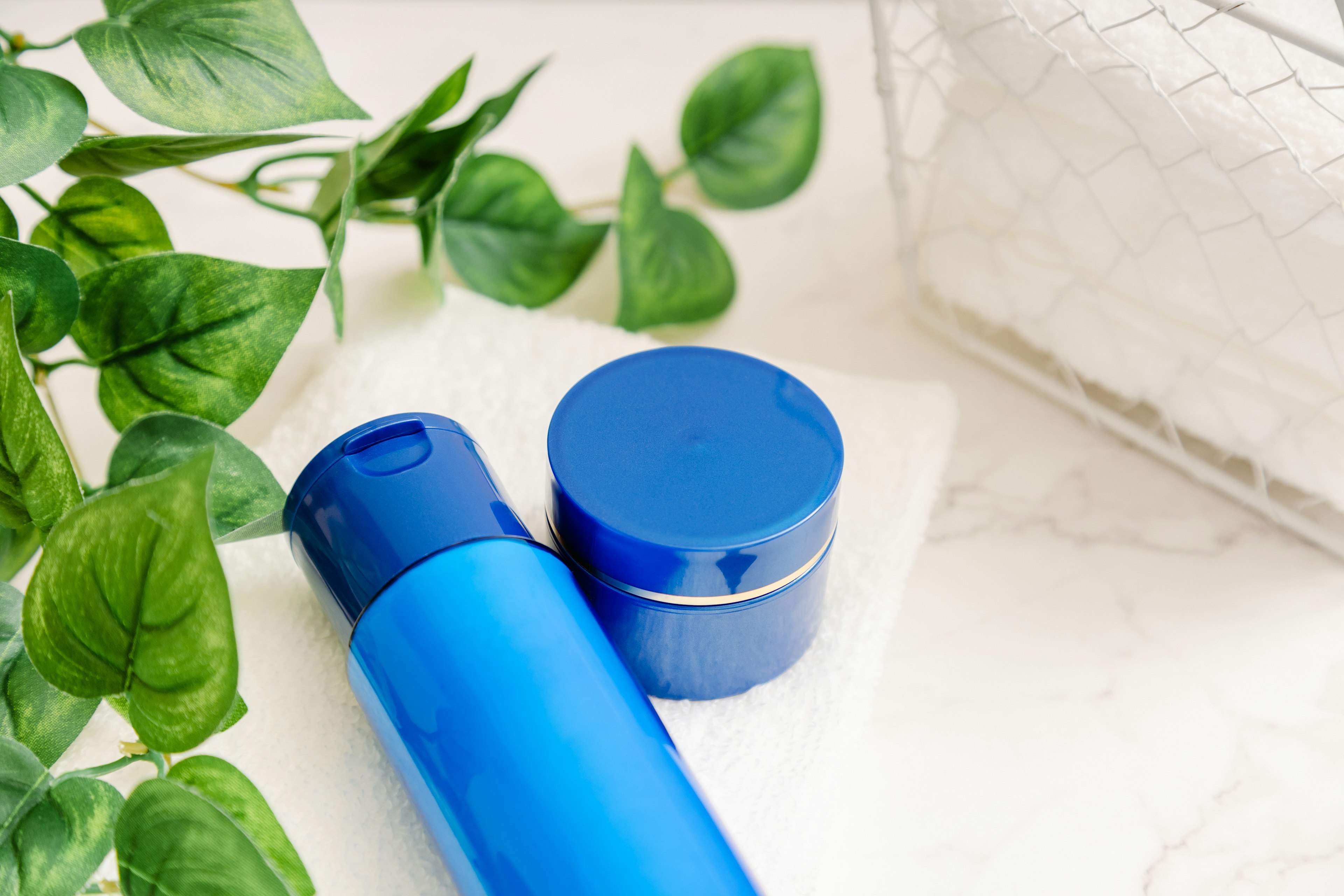 Imagen de botellas de cosméticos azules y un tarro de crema con plantas verdes de fondo