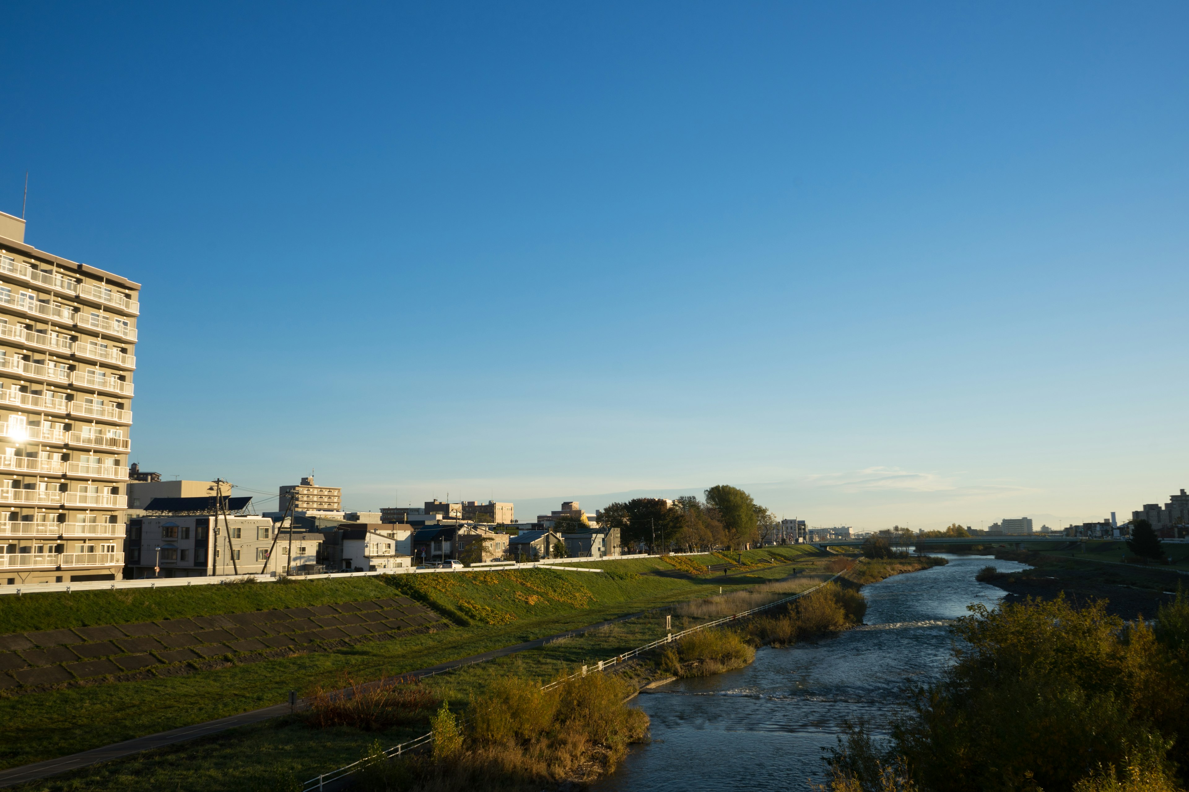 Paesaggio urbano con un fiume e erba verde sotto un cielo blu