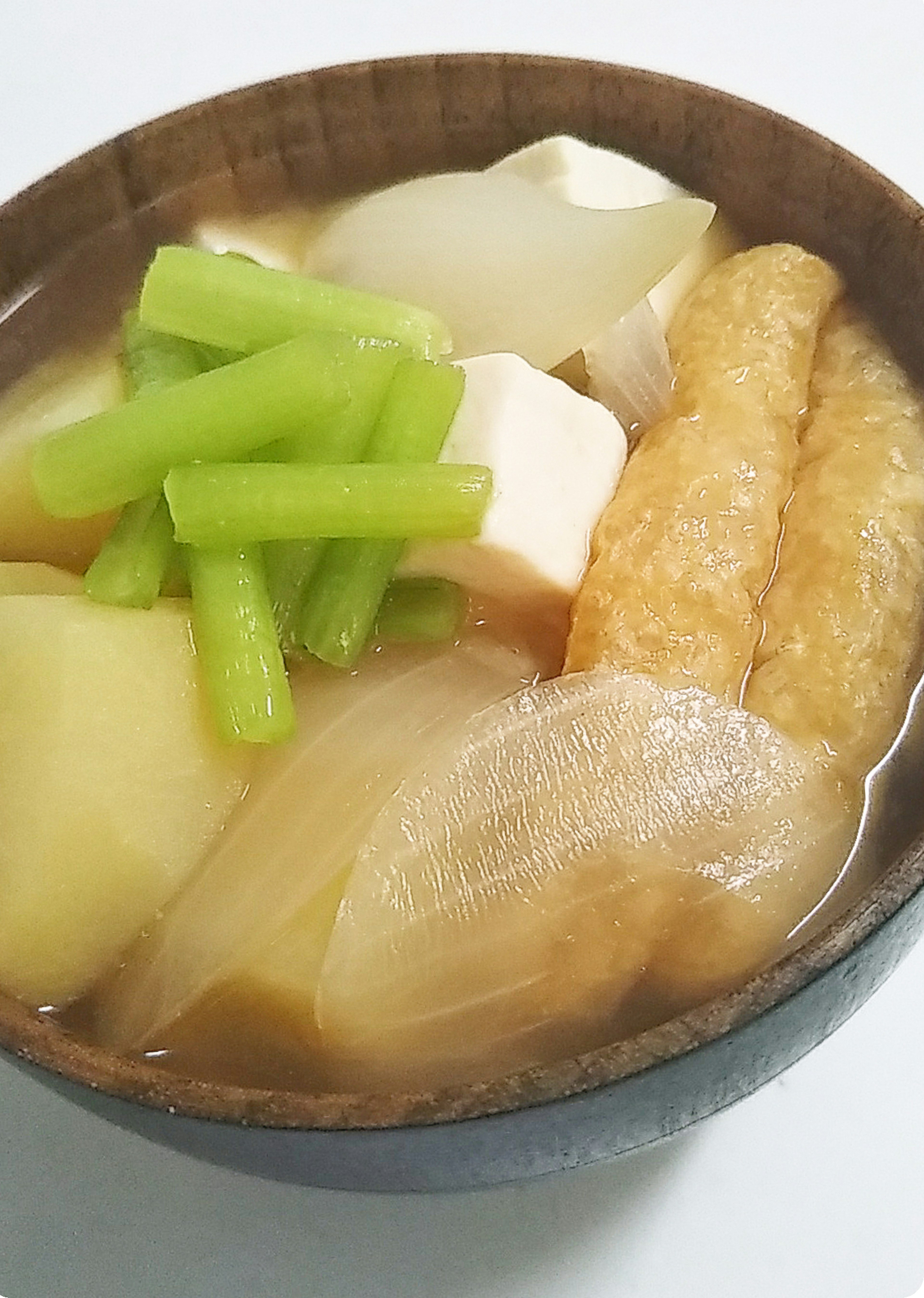 Ciotola di zuppa con vari ingredienti tra cui tofu bianco daikon morbido sedano verde e torta di pesce