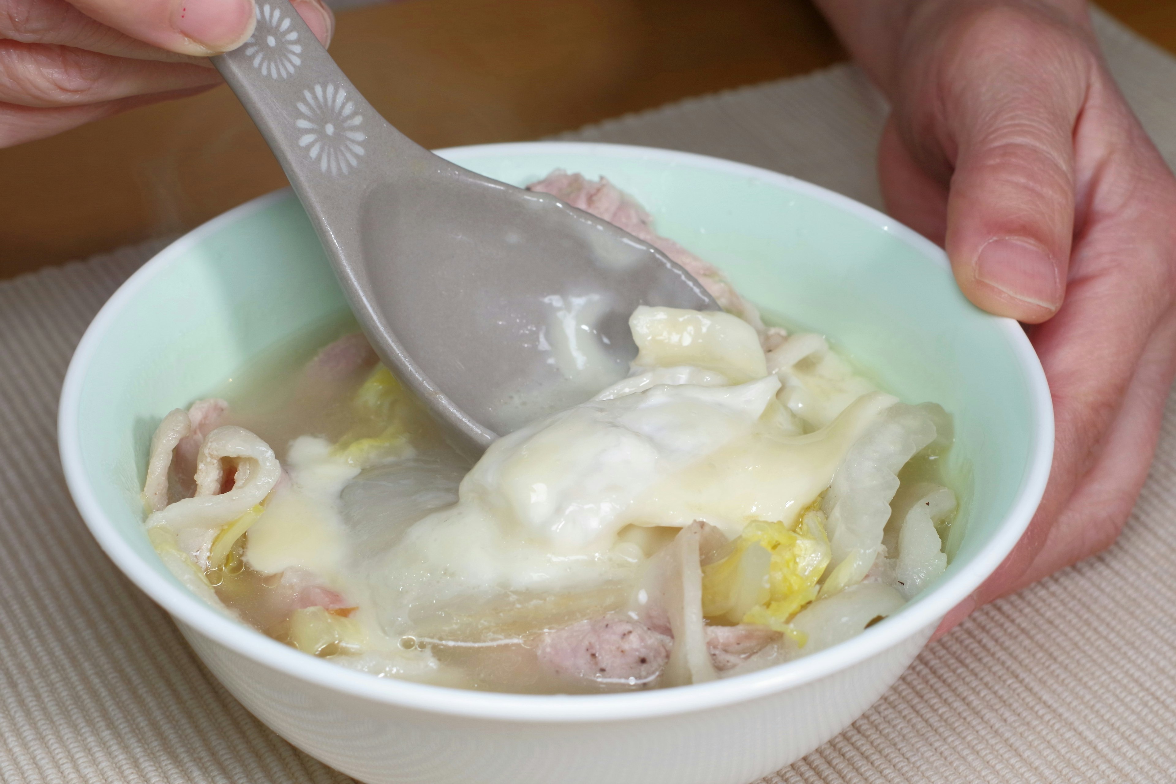 A hand holding a spoon scooping soup from a light green bowl