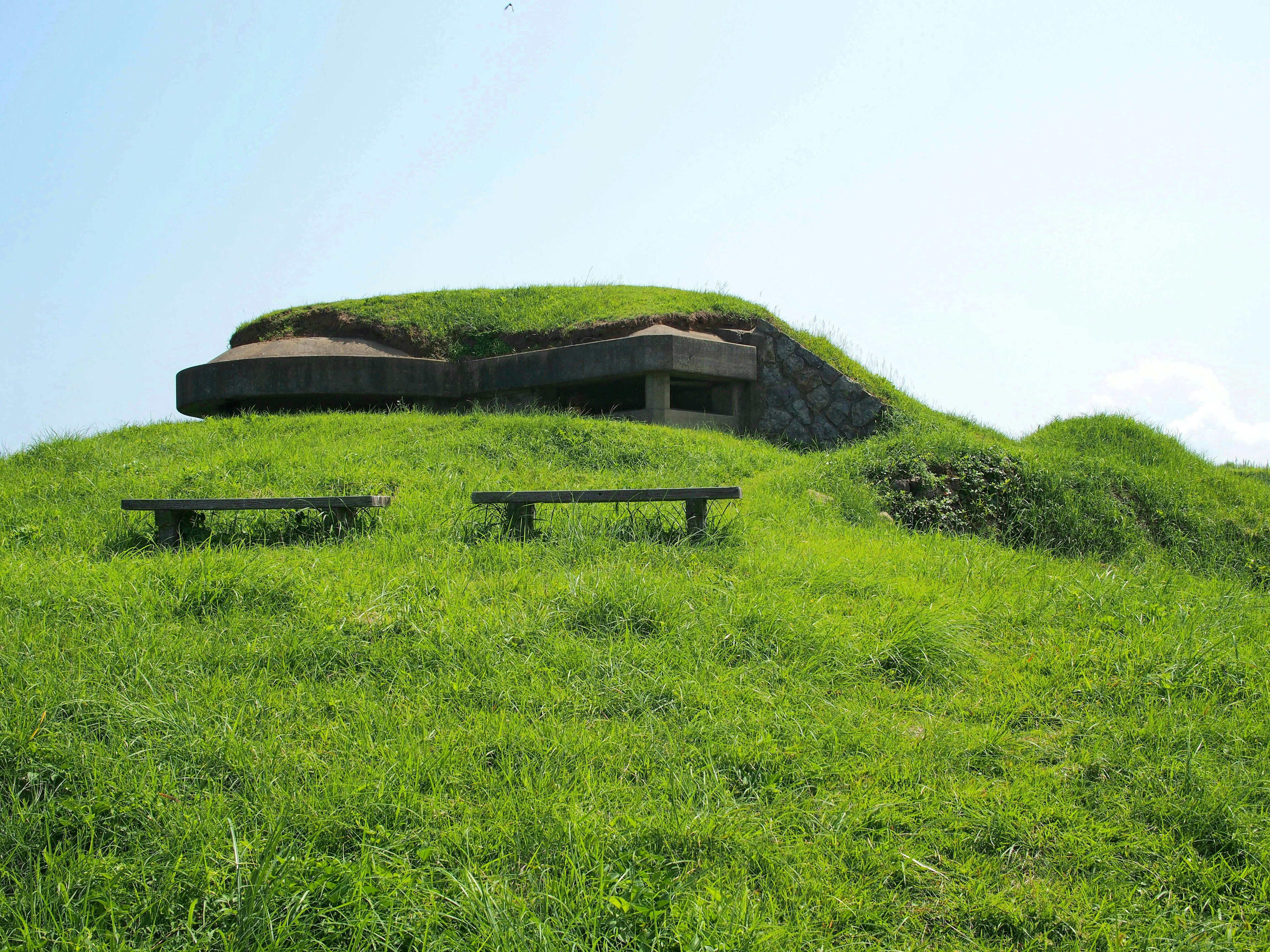 Tumulus ancien avec un abri au sommet entouré d'herbe verte luxuriante et de bancs