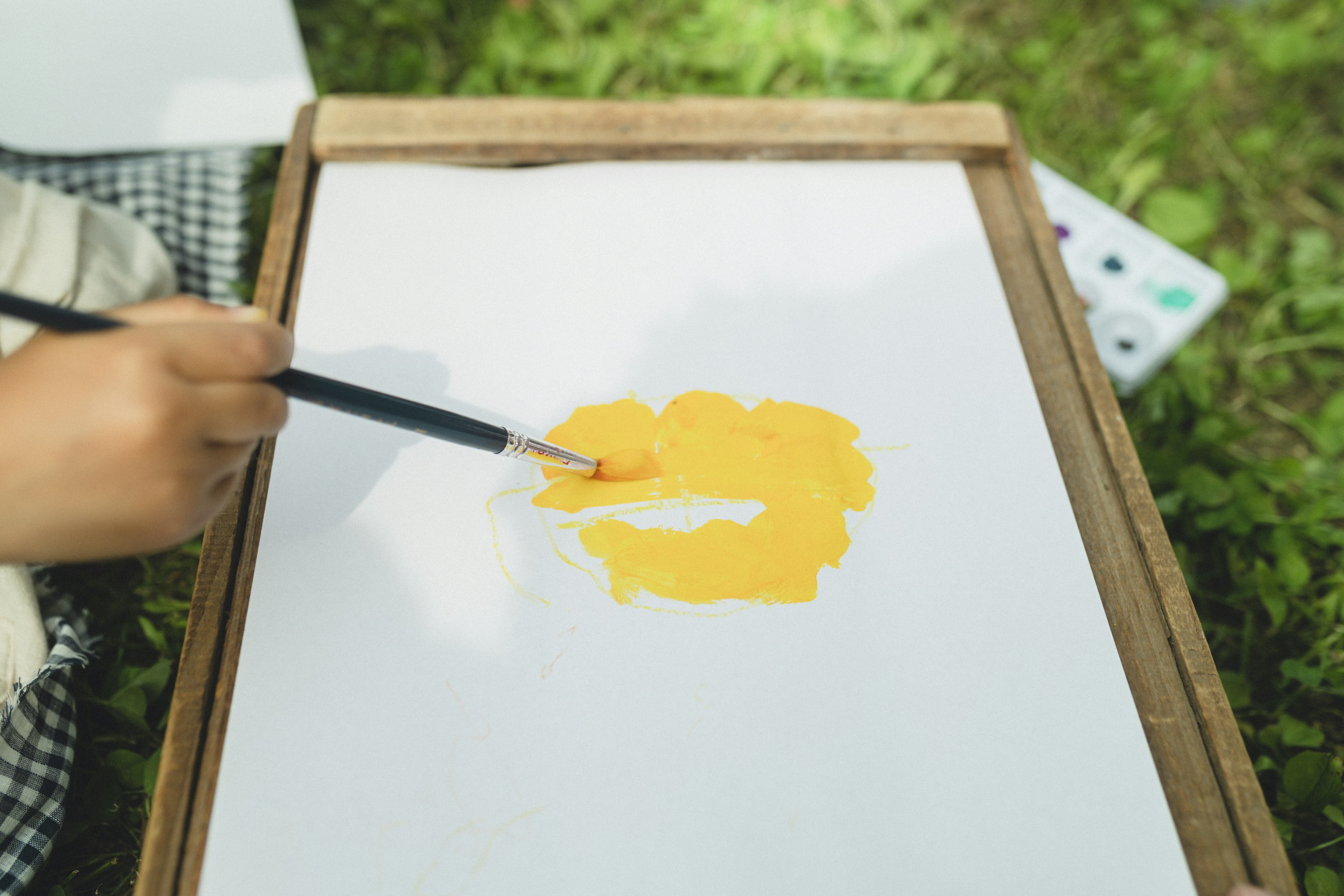 A hand painting a yellow shape on a white canvas outdoors