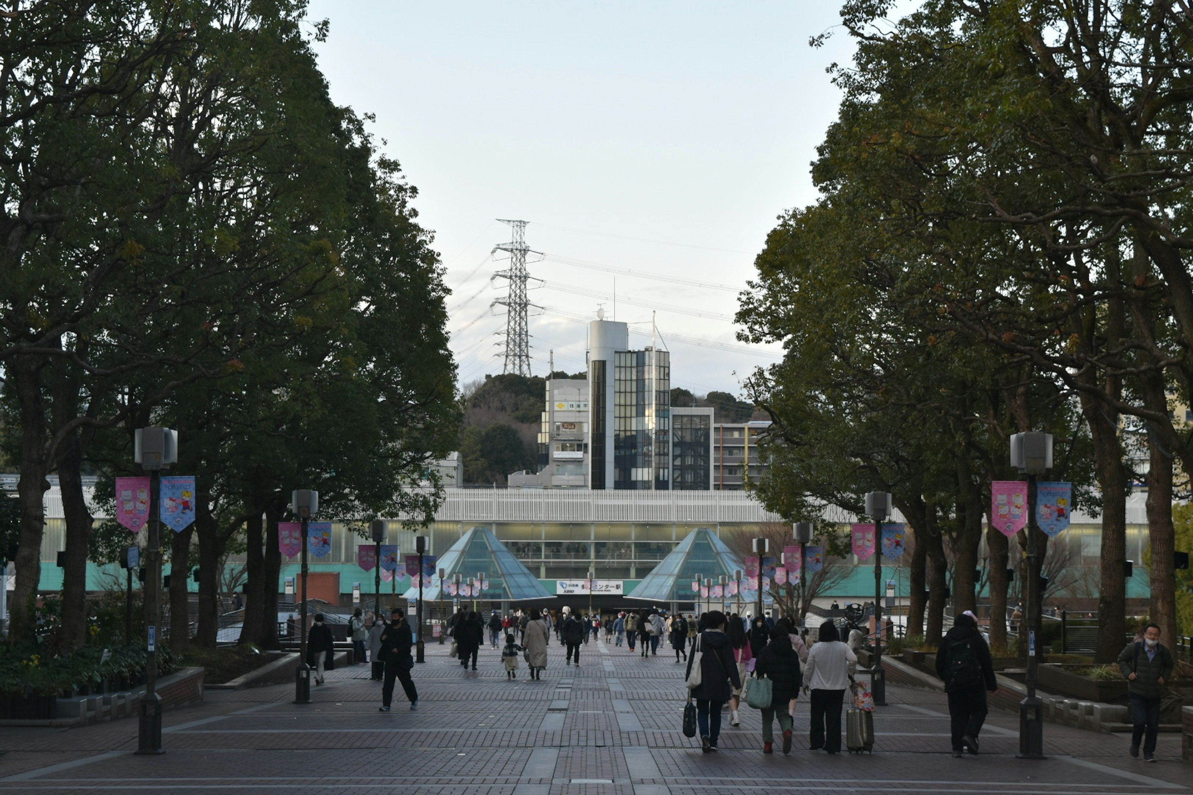 Una scena di persone che camminano lungo una strada alberata con edifici moderni sullo sfondo