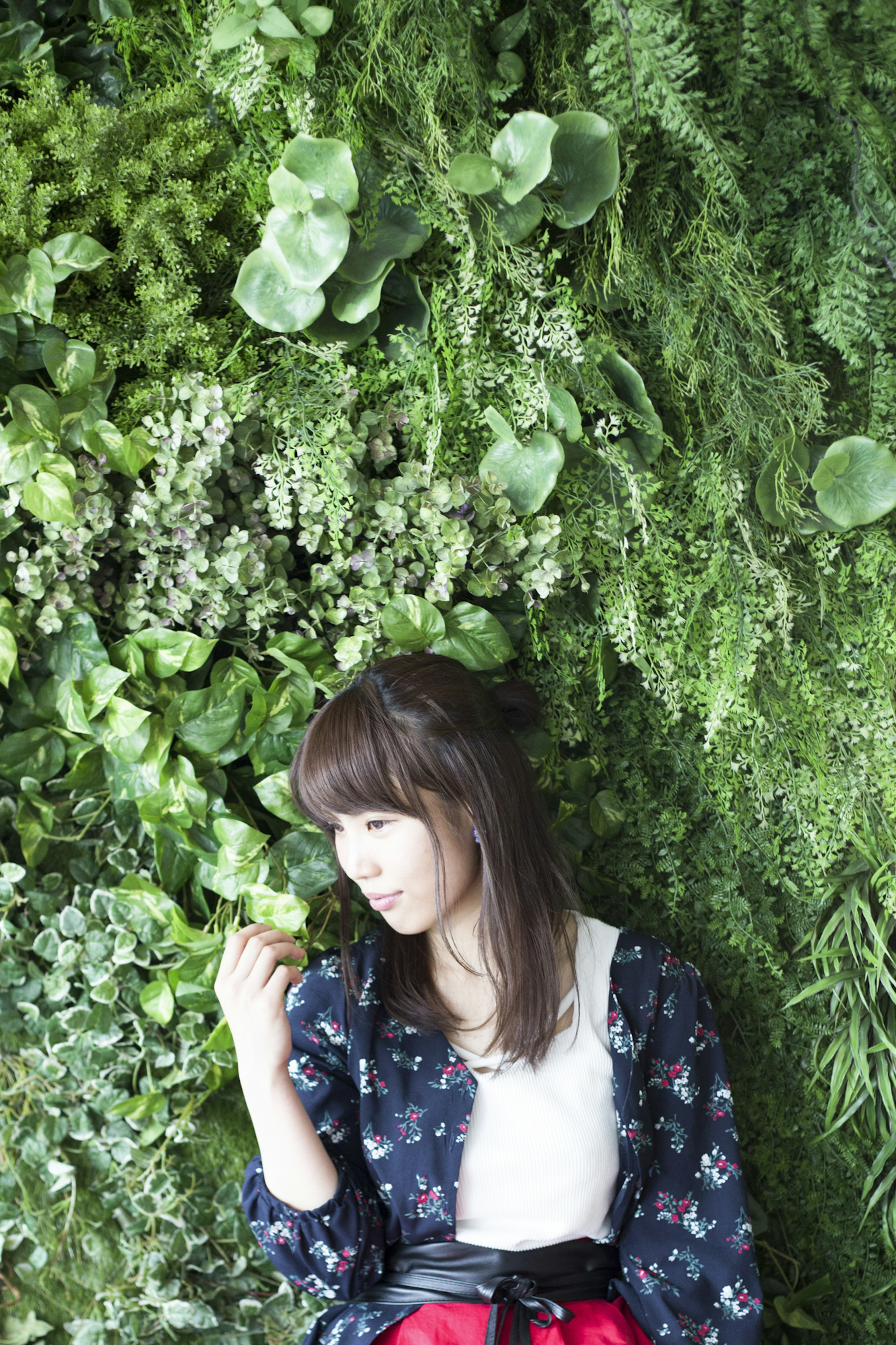 Portrait d'une femme devant un mur vert rempli de plantes diverses elle sourit de manière enjouée