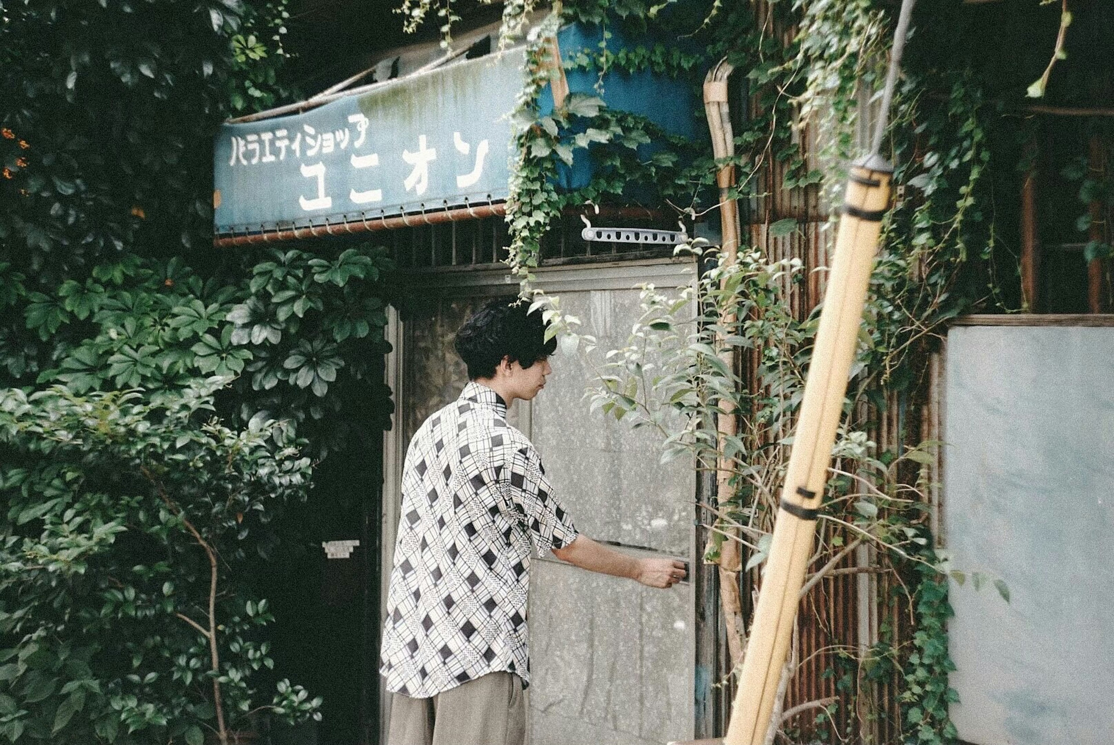 A young person standing in front of an old building surrounded by greenery reaching for the door