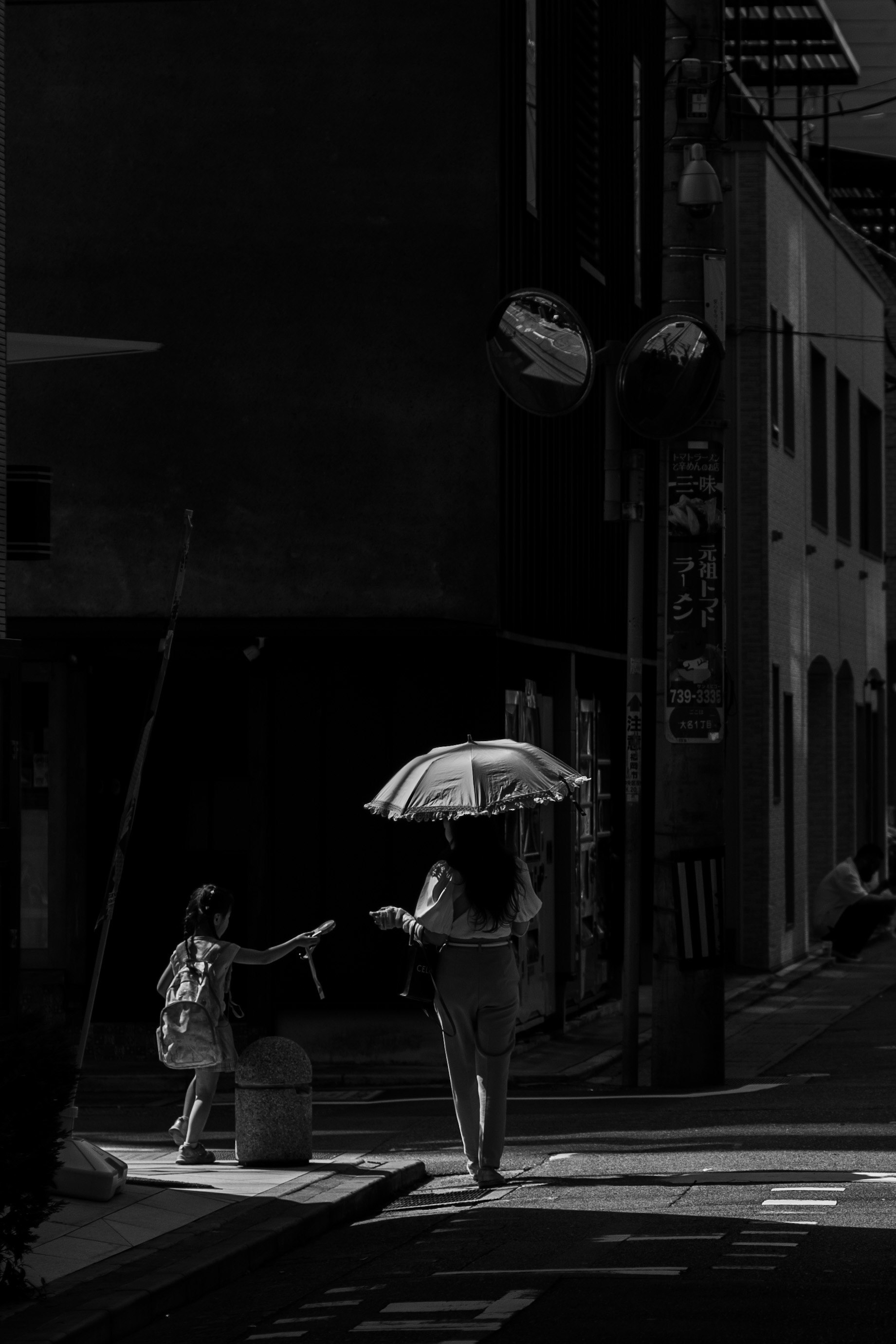 Silhouette of a woman walking with an umbrella at a street corner with a child