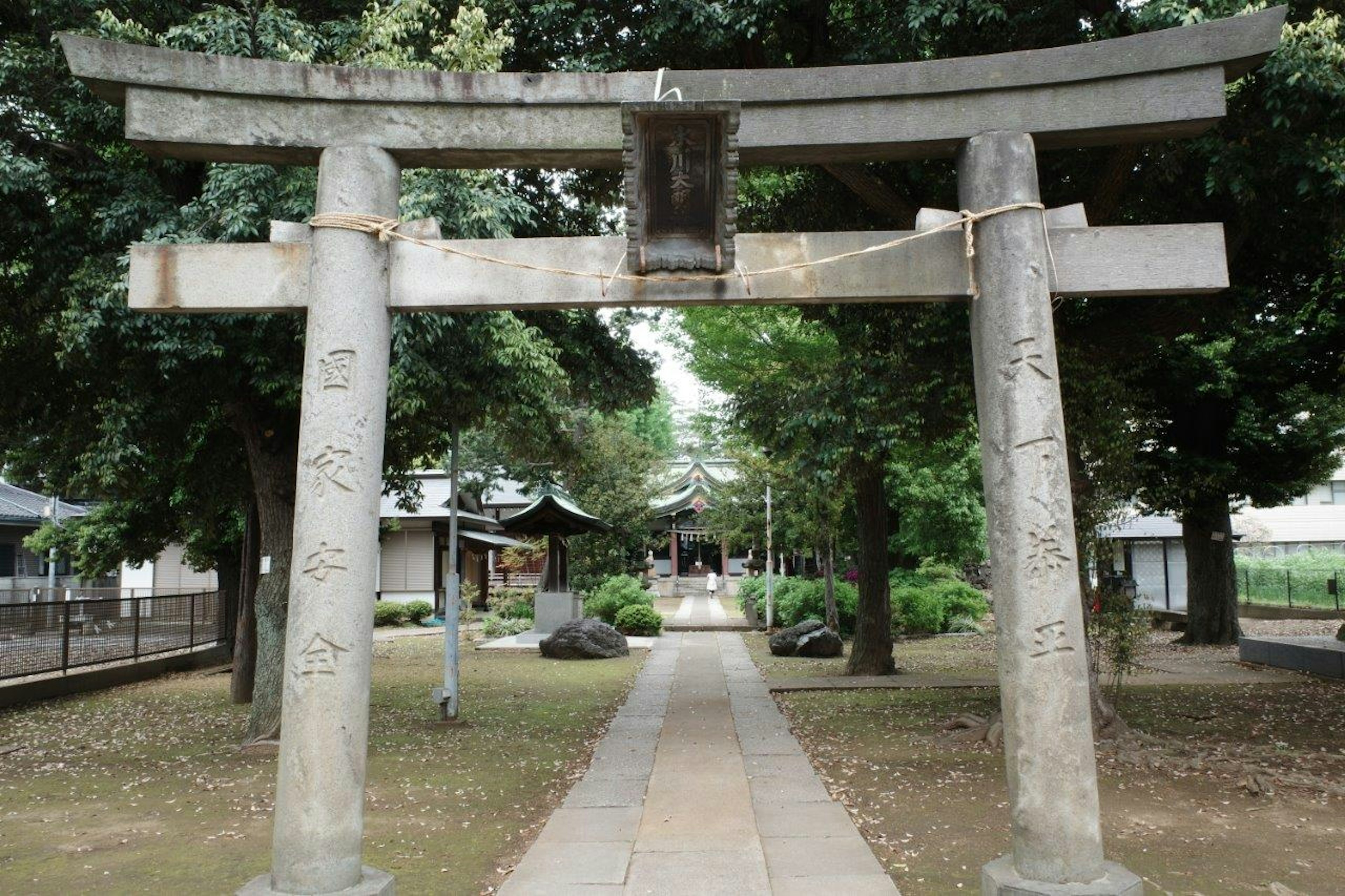 Stone torii gate at the entrance of a shrine surrounded by green trees along a pathway